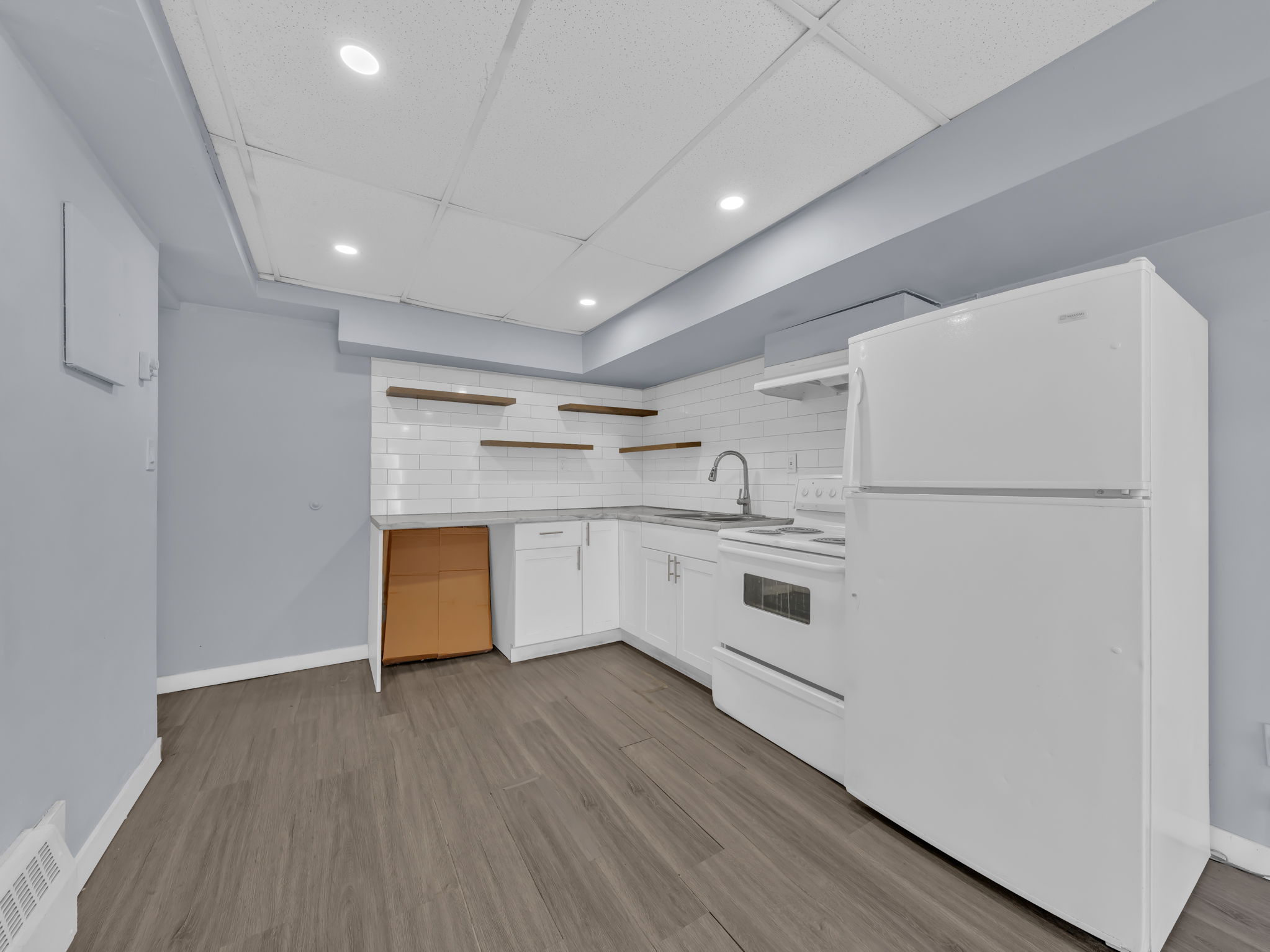 Kitchen with white cabinetry, tile backsplash, wooden floating shelves, and recessed lighting