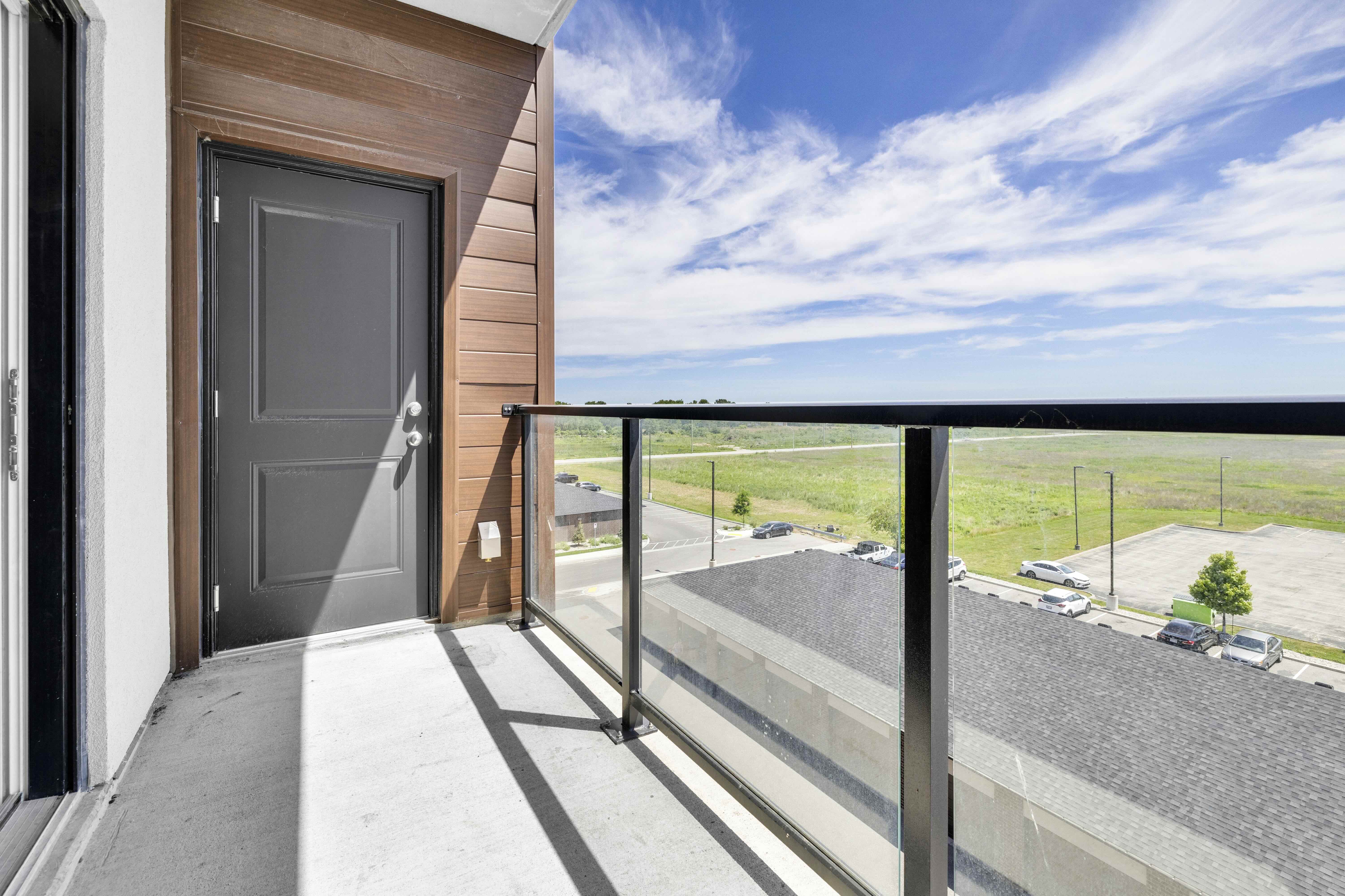 East-facing balcony with glass railing, black door, and wood-paneled wall under open sky