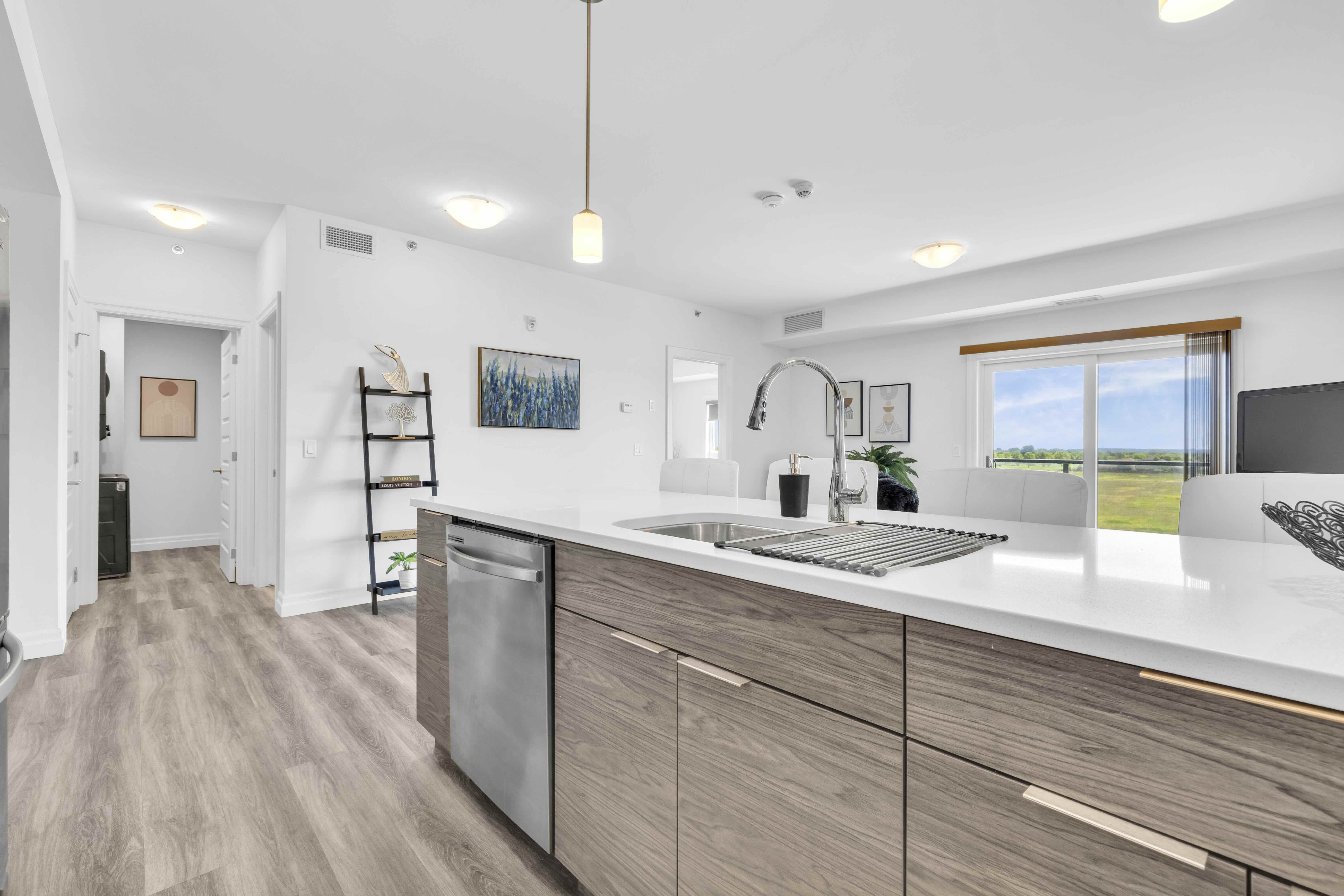 Kitchen island side angle with sink, dishwasher, and view to living area and balcony window