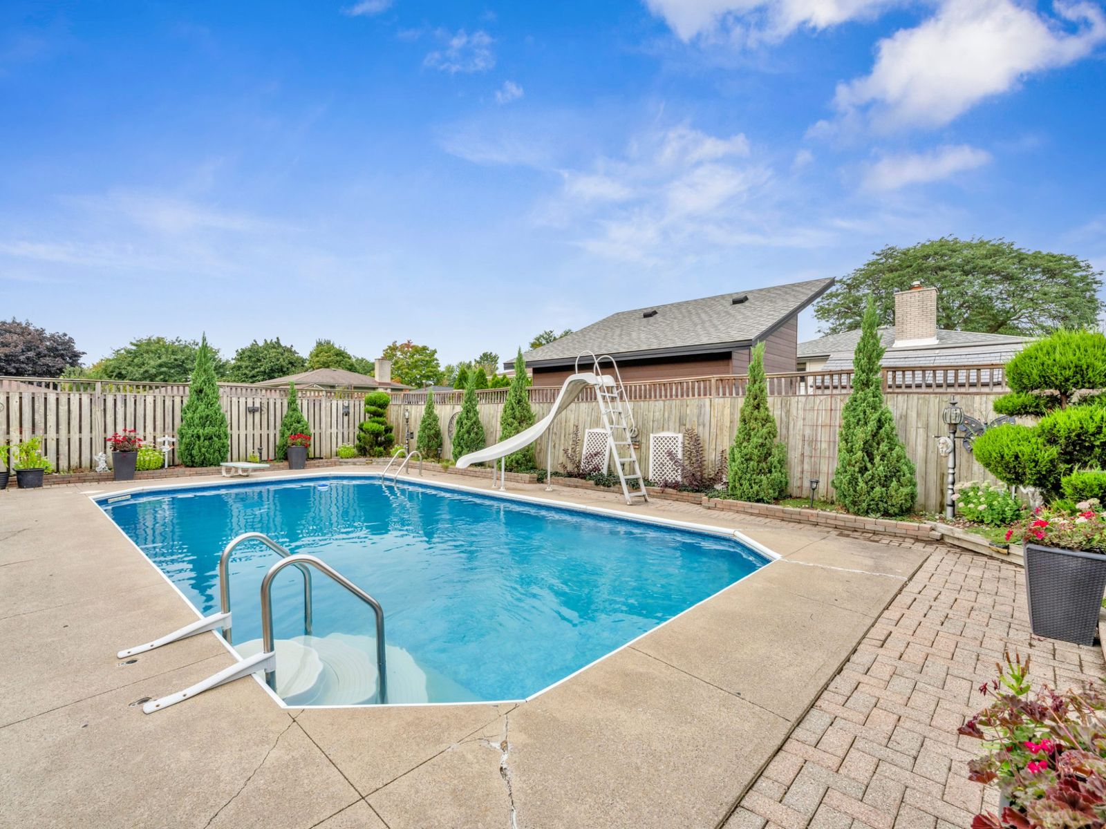 The pool from the patio side, with the paver walkway, plants and fence.