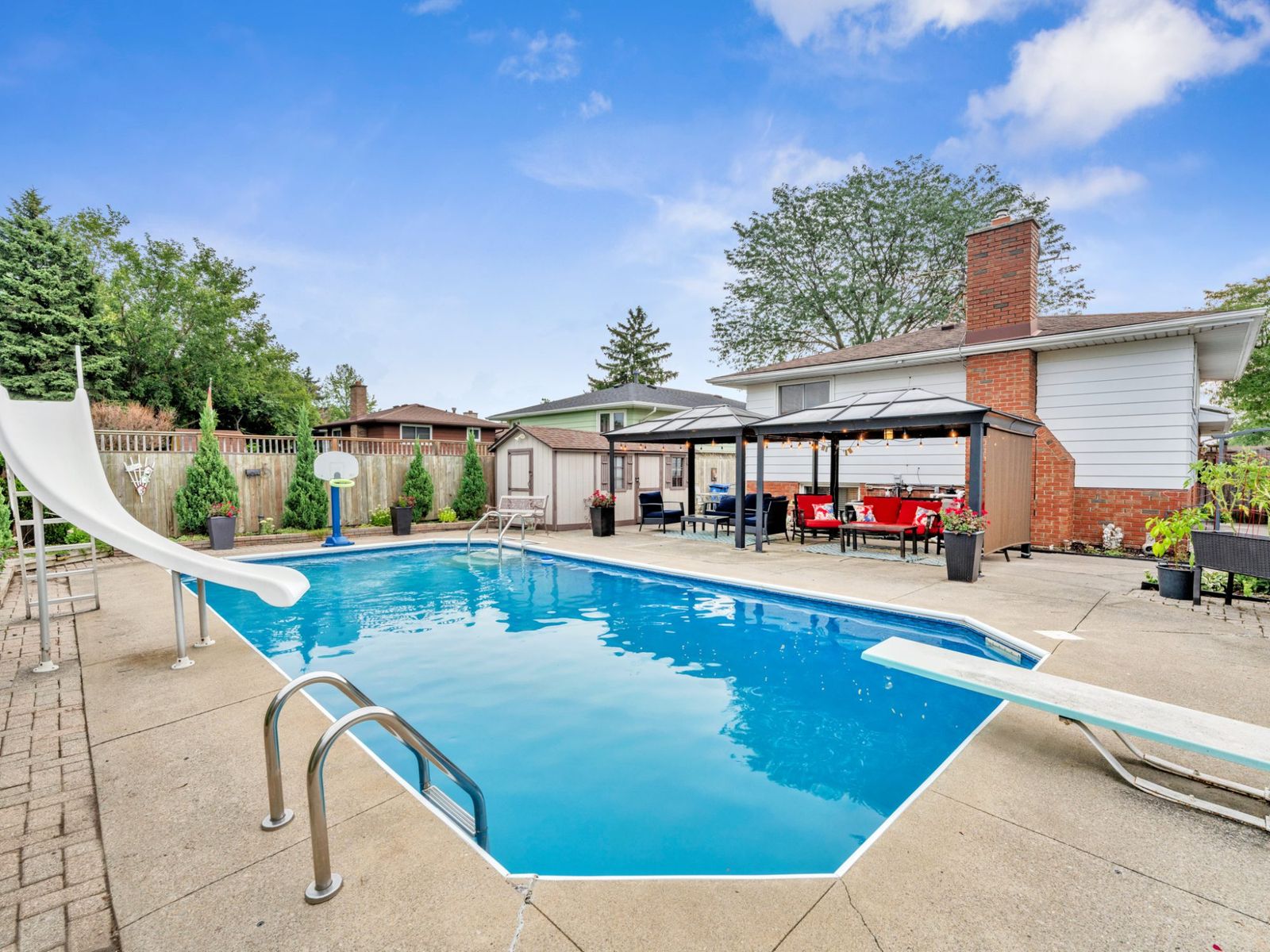 The inground pool with the slide, diving board and covered gazebos beyond.