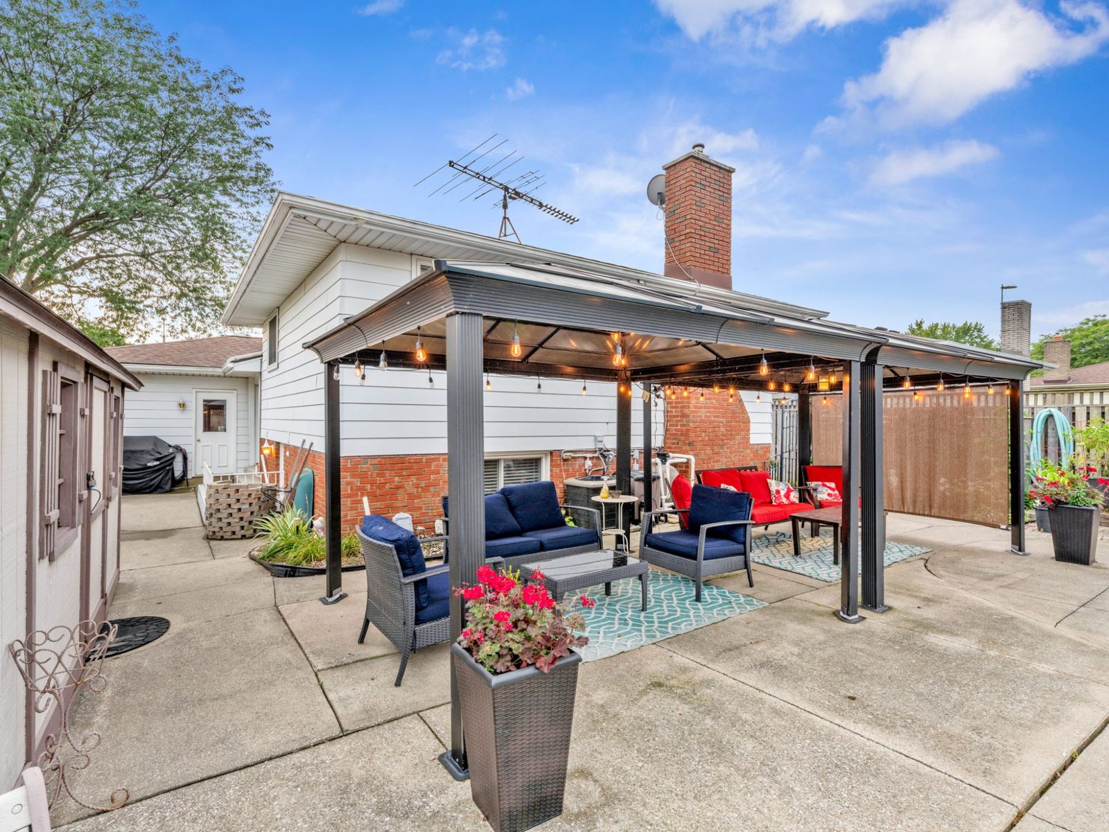 A covered gazebo with string lights and seating on the patio beside the house.