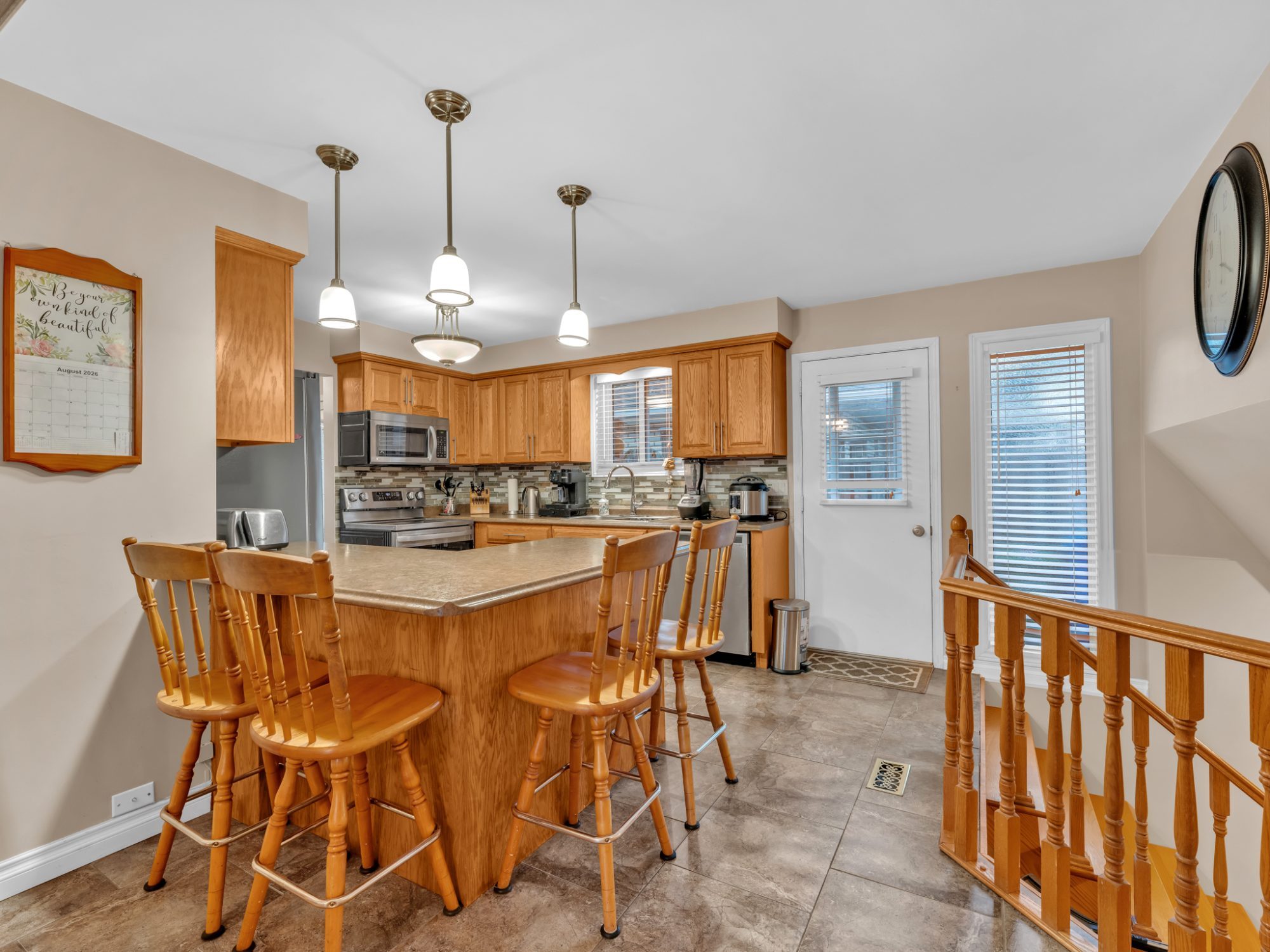 The kitchen island with three bar stools, pendant lights and stainless appliances.