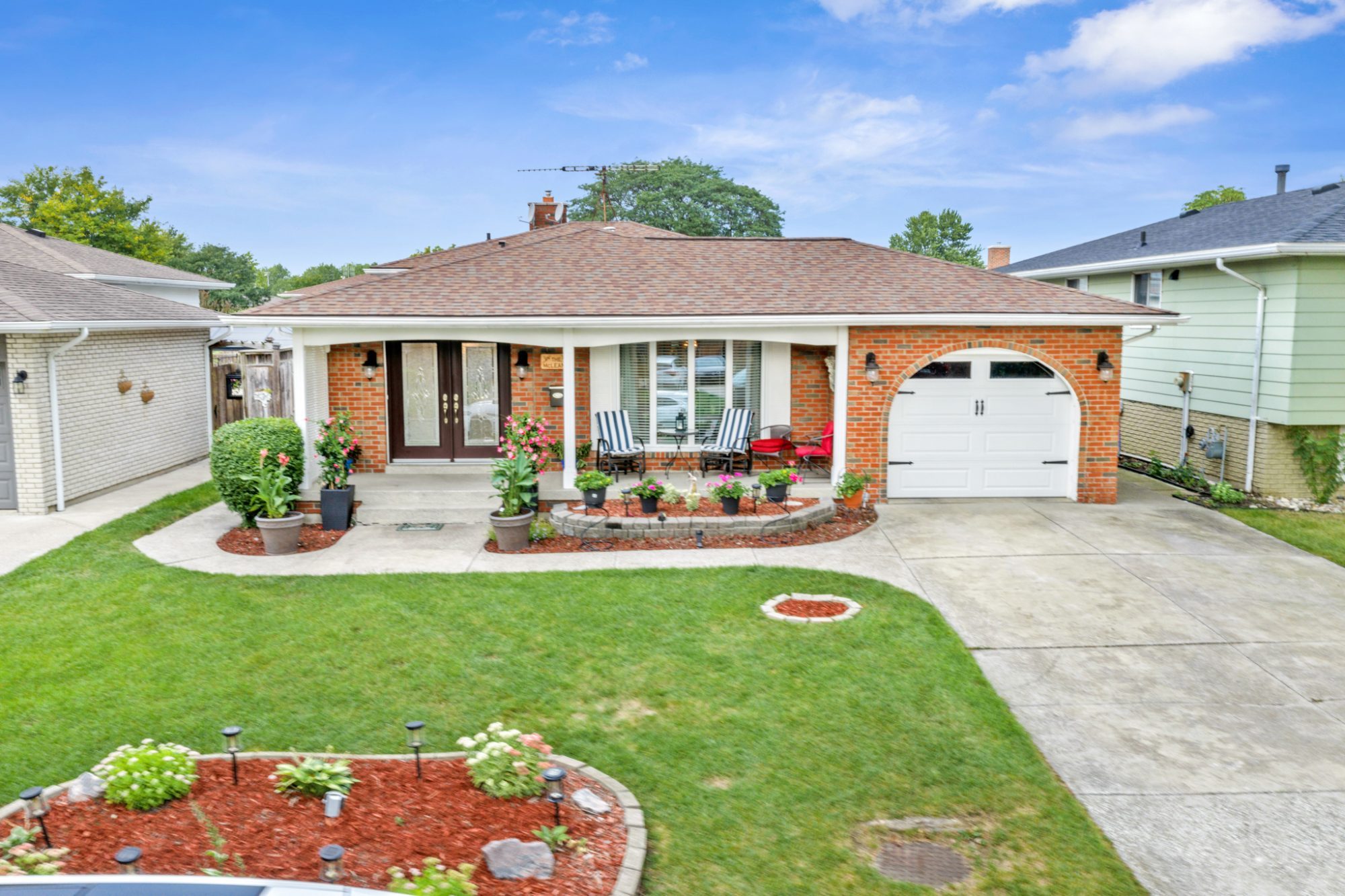 The front of 9975 Holly Crescent: brick, a covered porch, an arched single garage and a landscaped lawn.