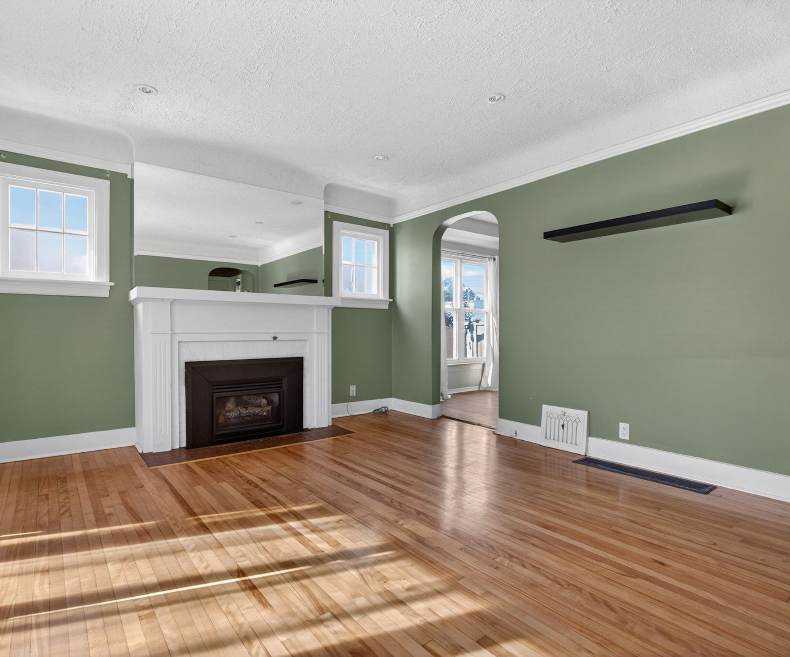 Wide view of living room with hardwood floors, green walls, and arched doorway