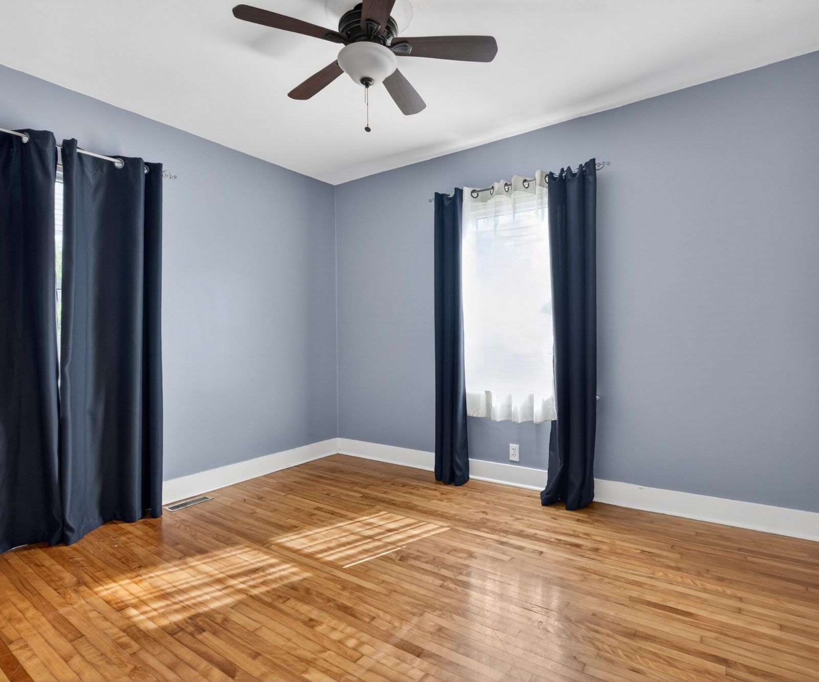 Bedroom with ceiling fan, two windows, hardwood floor