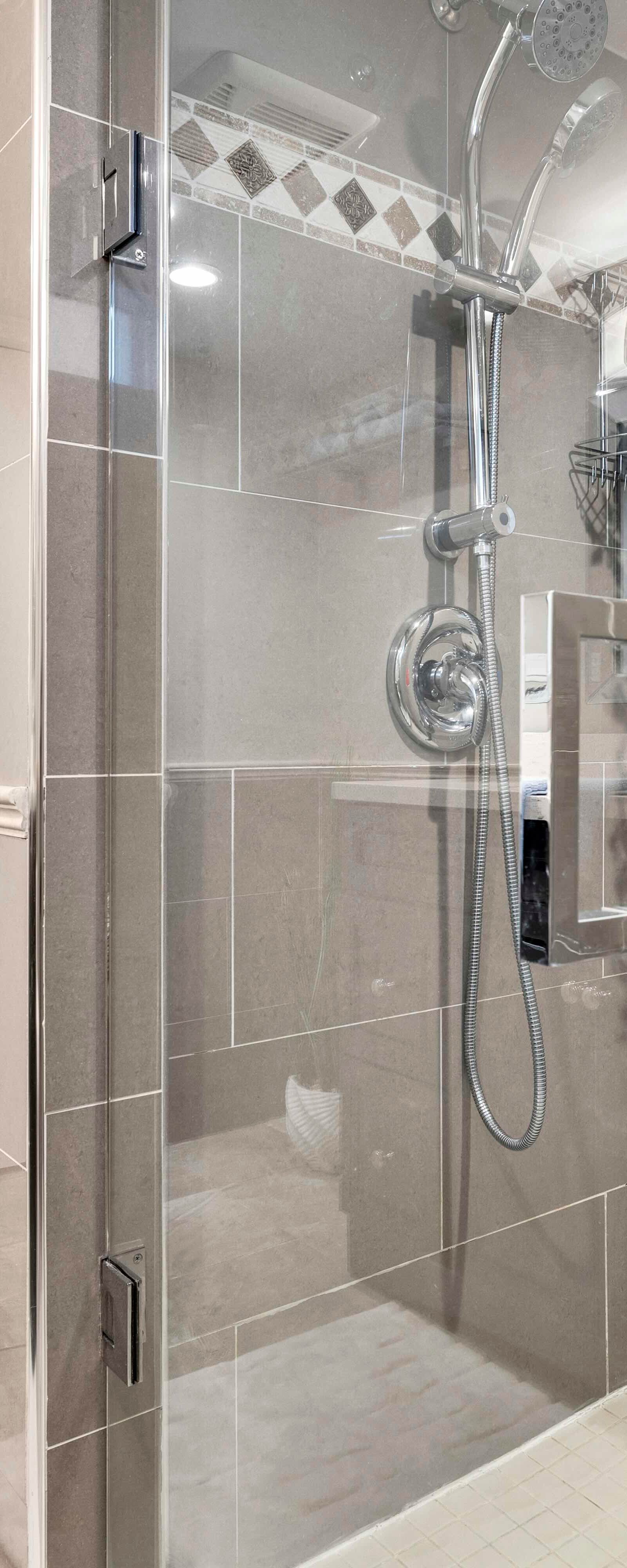 Glass-enclosed shower with decorative tiles and grab bar next to a closet with white doors in a bathroom.