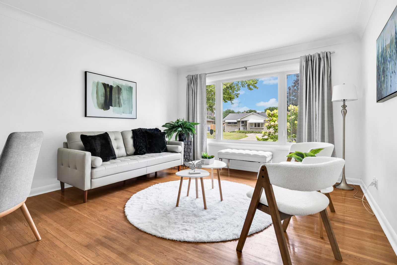 Living room featuring sofa, chairs, and large window with view to outside houses and greenery.