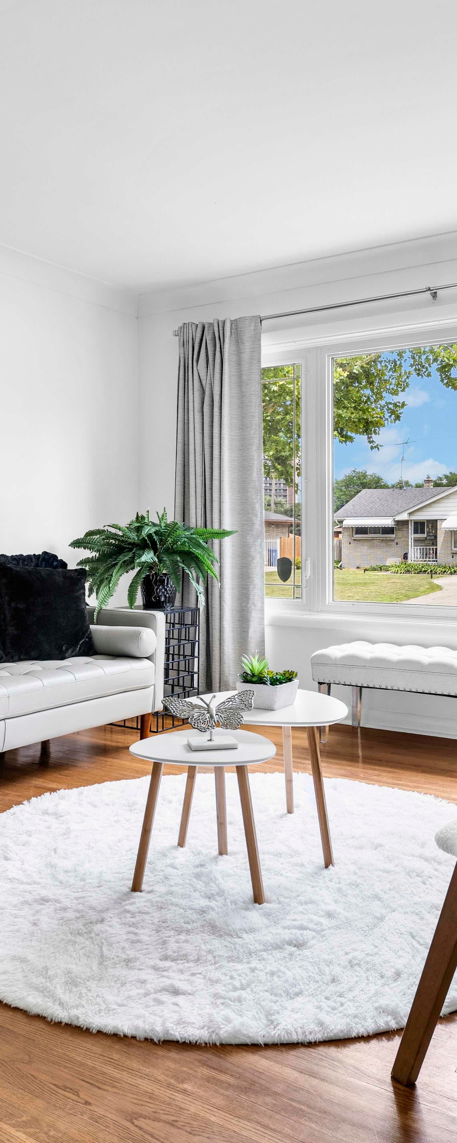 Living room featuring sofa, chairs, and large window with view to outside houses and greenery.