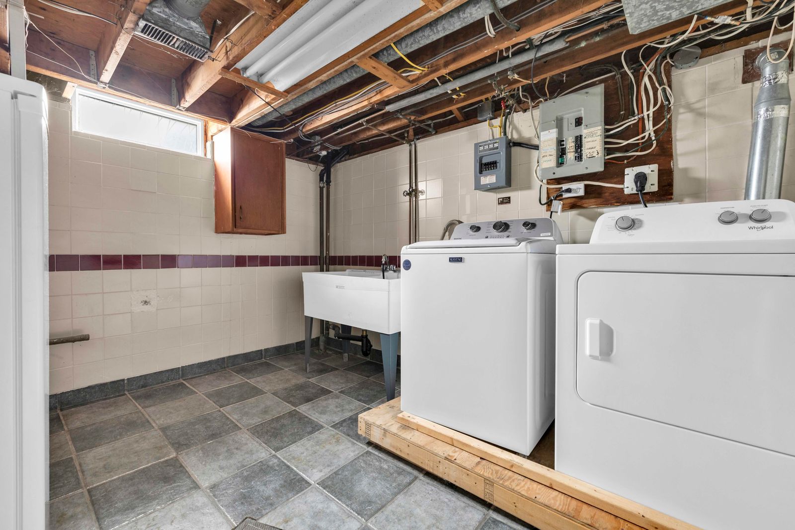Basement laundry room with washer, dryer, utility sink, tiled walls and floor.