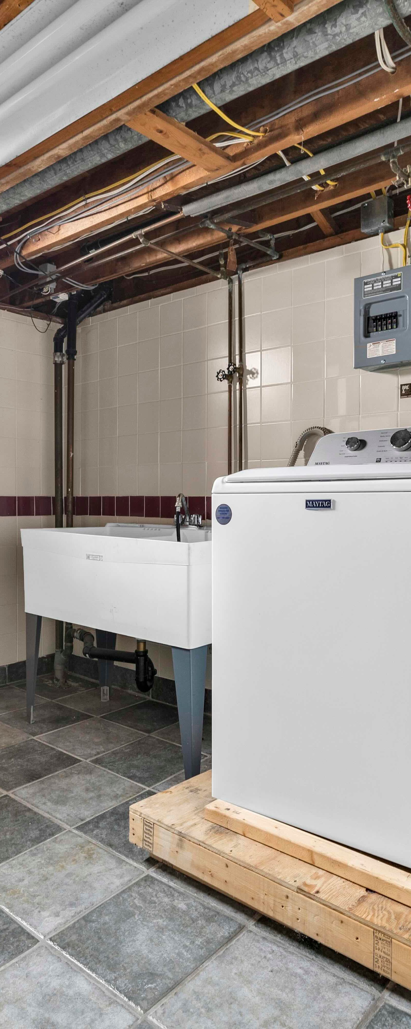 Basement laundry room with washer, dryer, utility sink, tiled walls and floor.