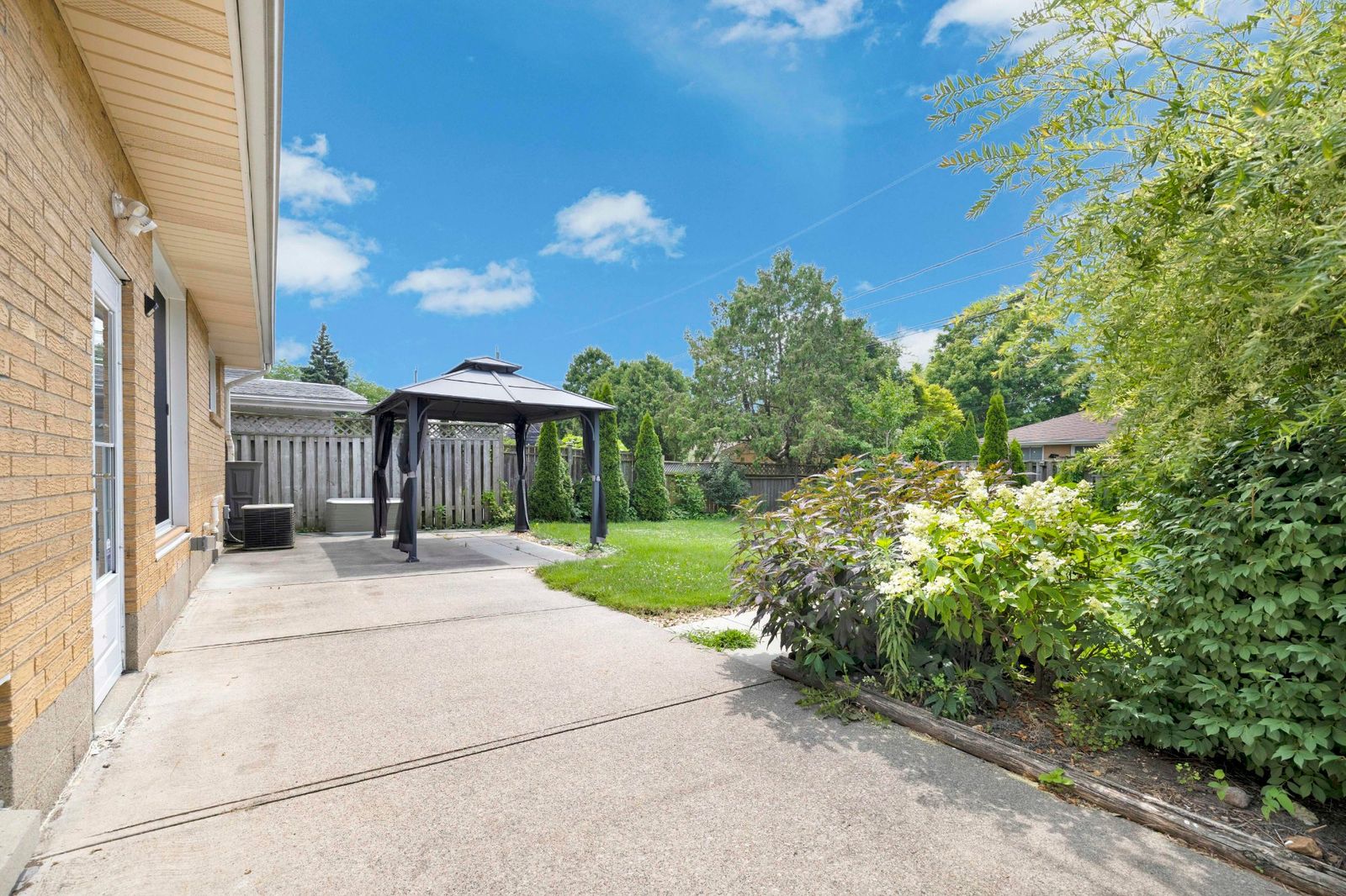 Concrete patio area at the rear of the house with gazebo, fence, and landscaping.