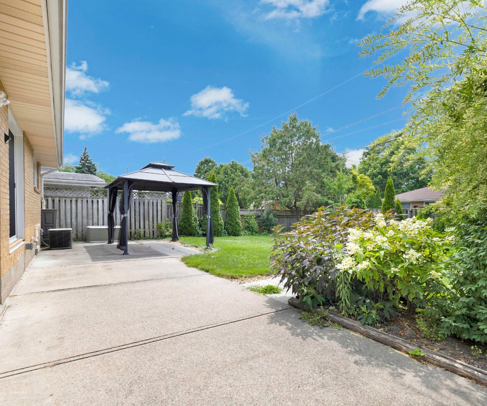 Concrete patio area at the rear of the house with gazebo, fence, and landscaping.