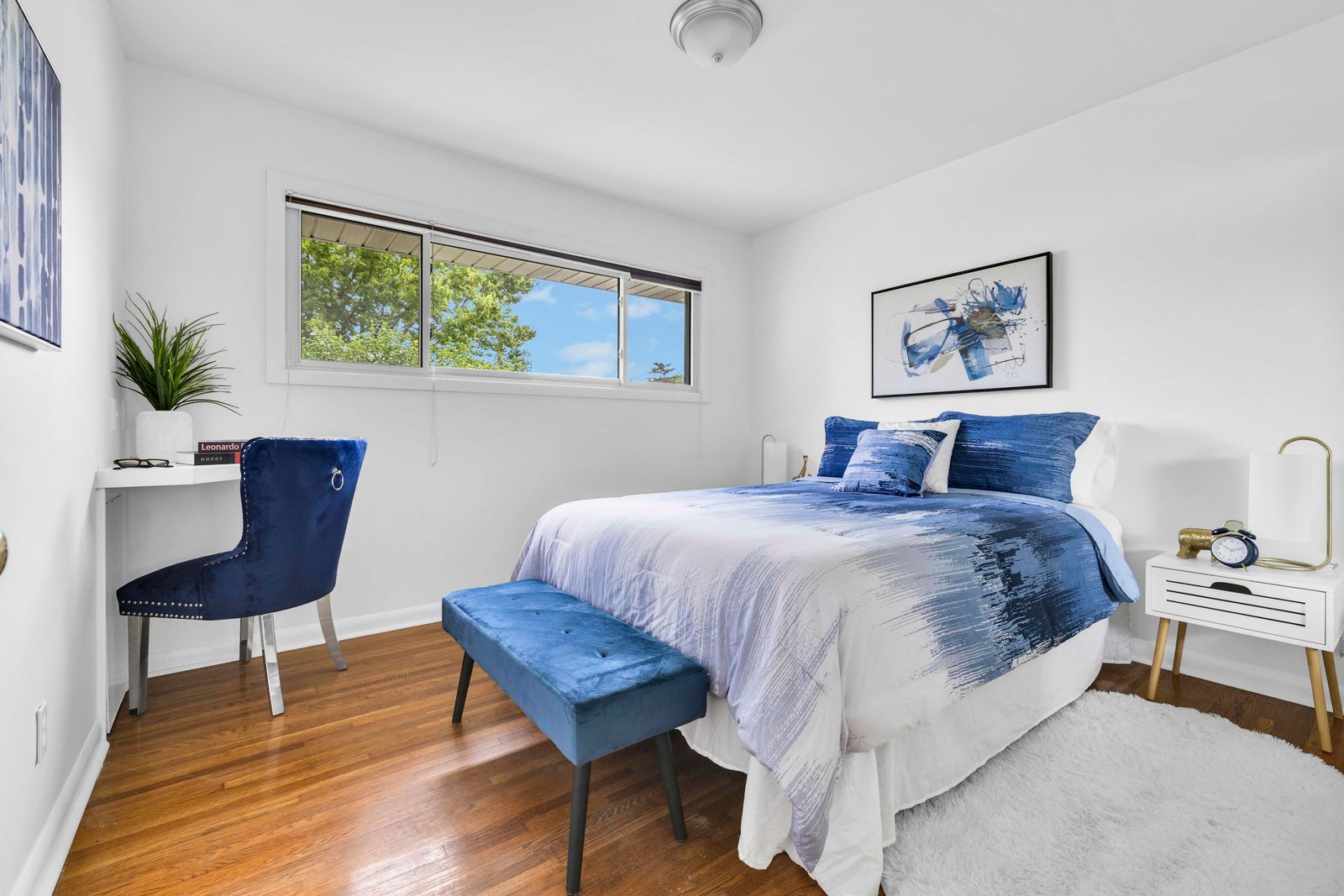 Bedroom featuring a bed with blue bedding, matching bench and chair, and bright window view.