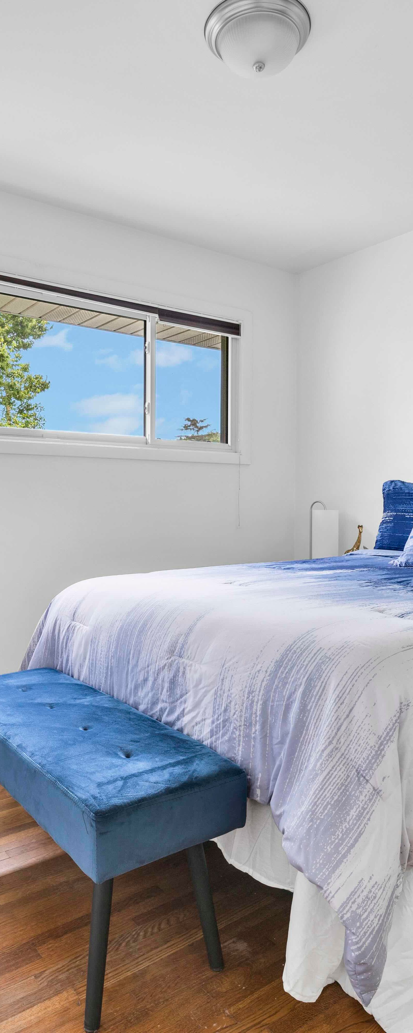 Bedroom featuring a bed with blue bedding, matching bench and chair, and bright window view.