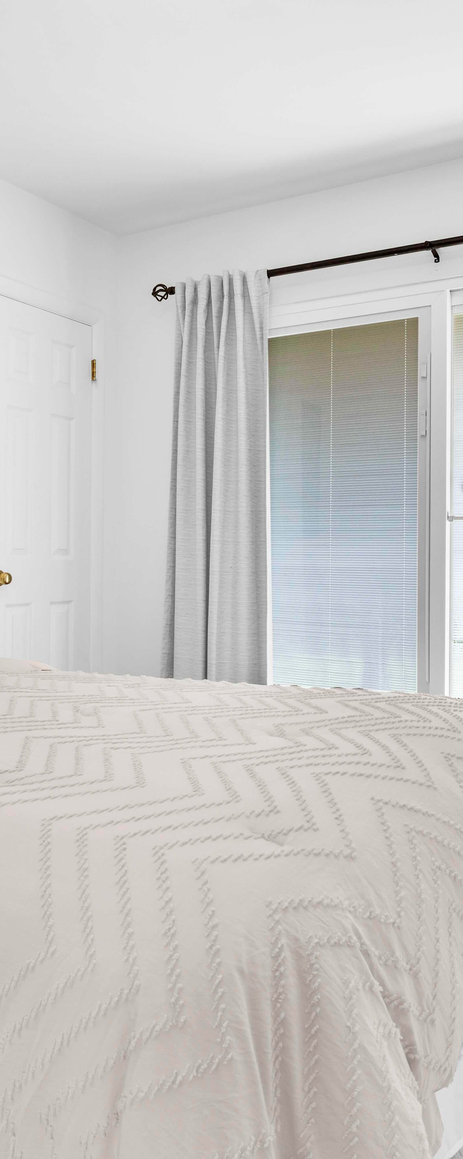 Primary bedroom with a beige bed, white walls, sliding glass door, and flooring.