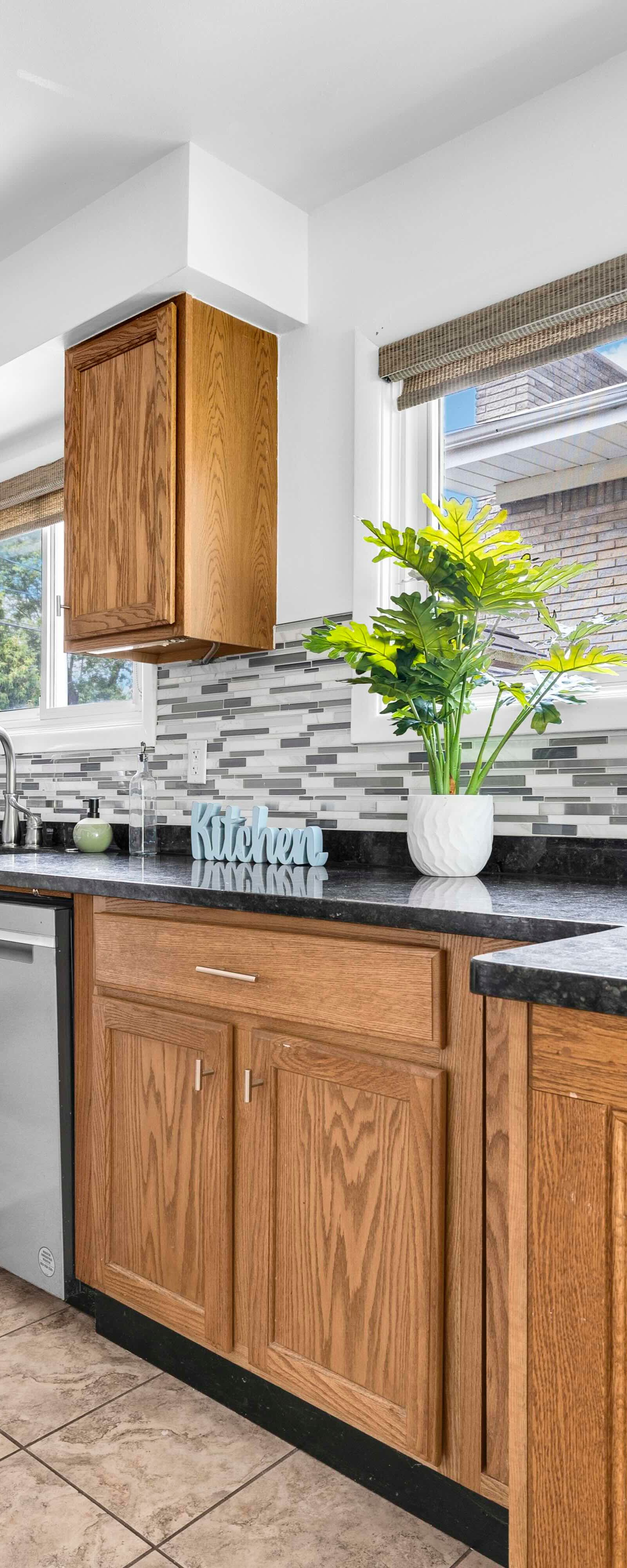 Kitchen with wooden cabinetry, black countertops, tiled backsplash, and appliances.