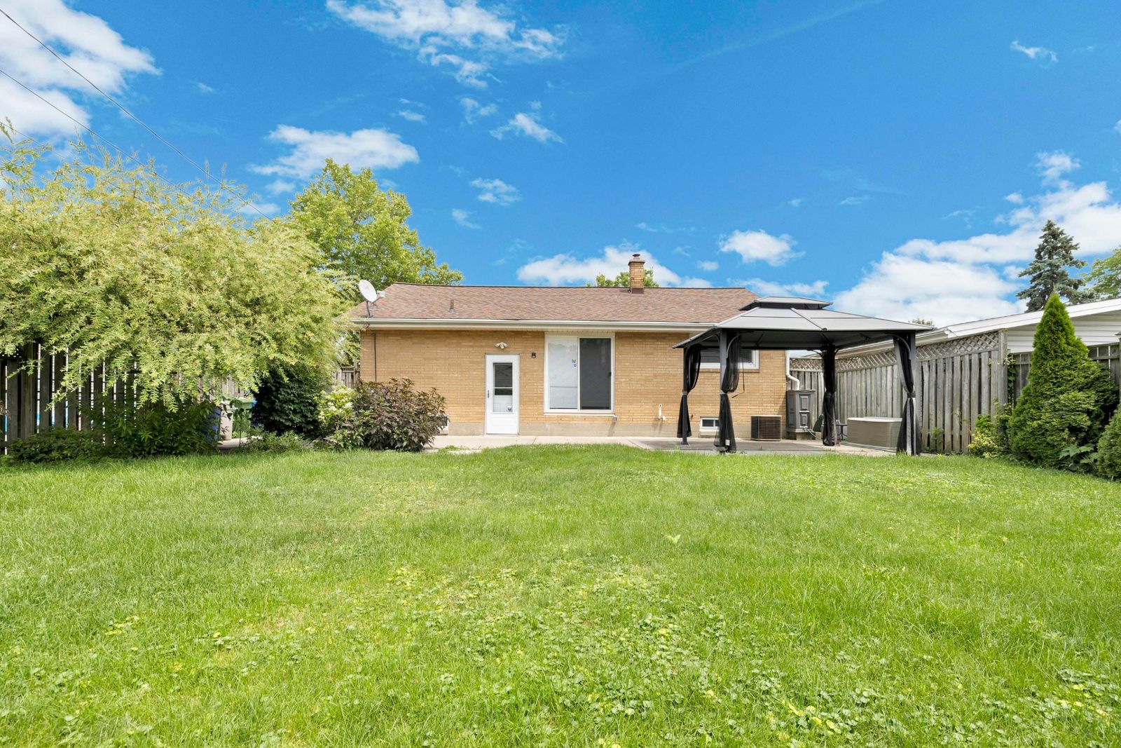 Wide rear exterior view of the house with grassy backyard, patio, gazebo, and wooden fence.