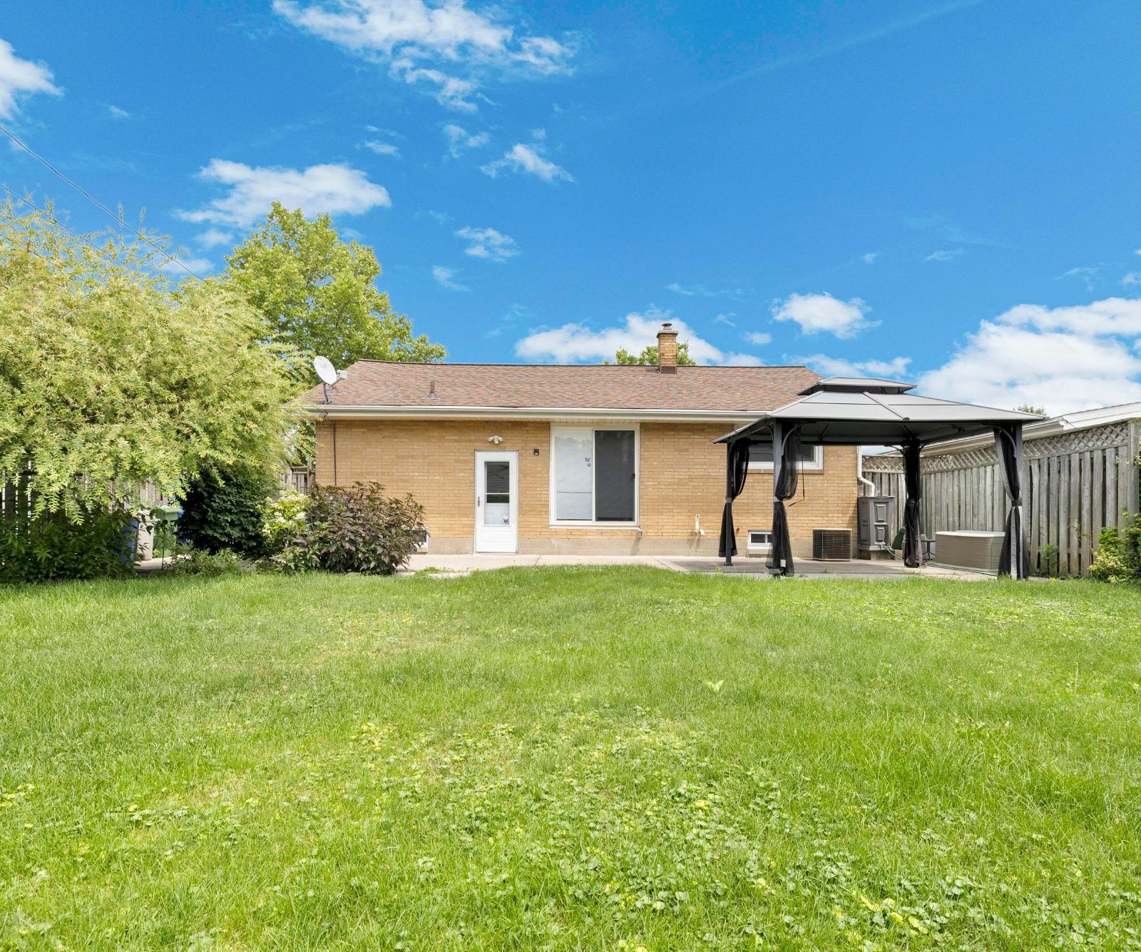 Wide rear exterior view of the house with grassy backyard, patio, gazebo, and wooden fence.