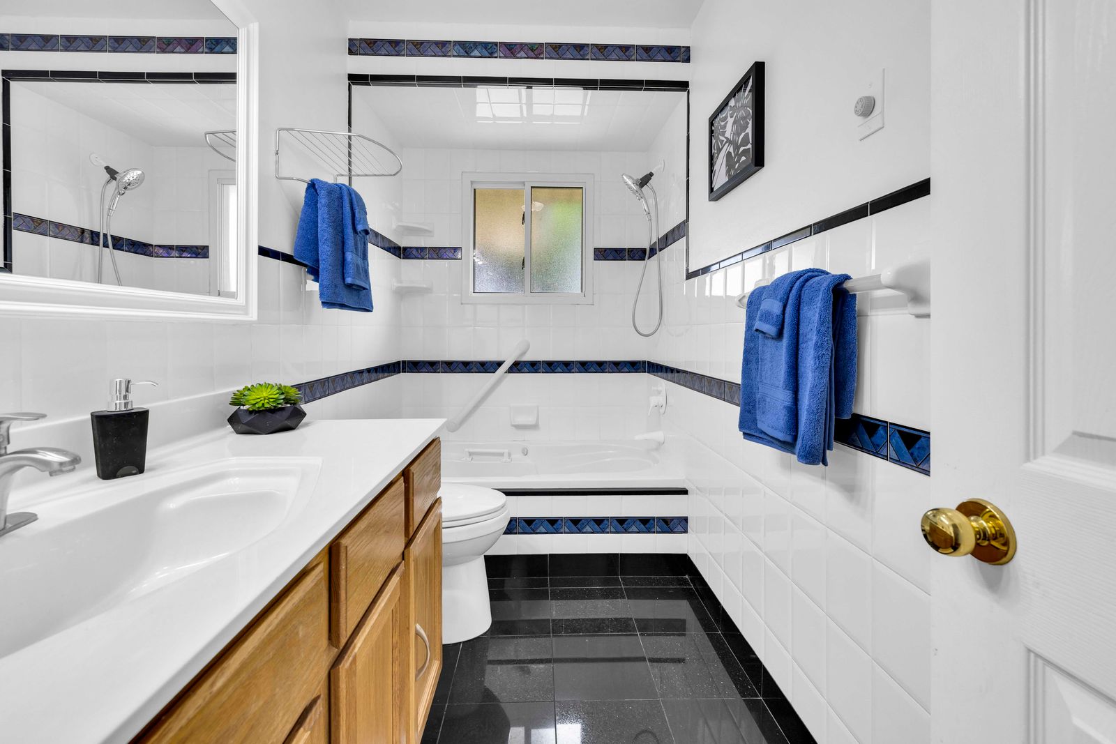 Bathroom with white tiles, blue trim, wood vanity, and a bathtub with double showerheads.
