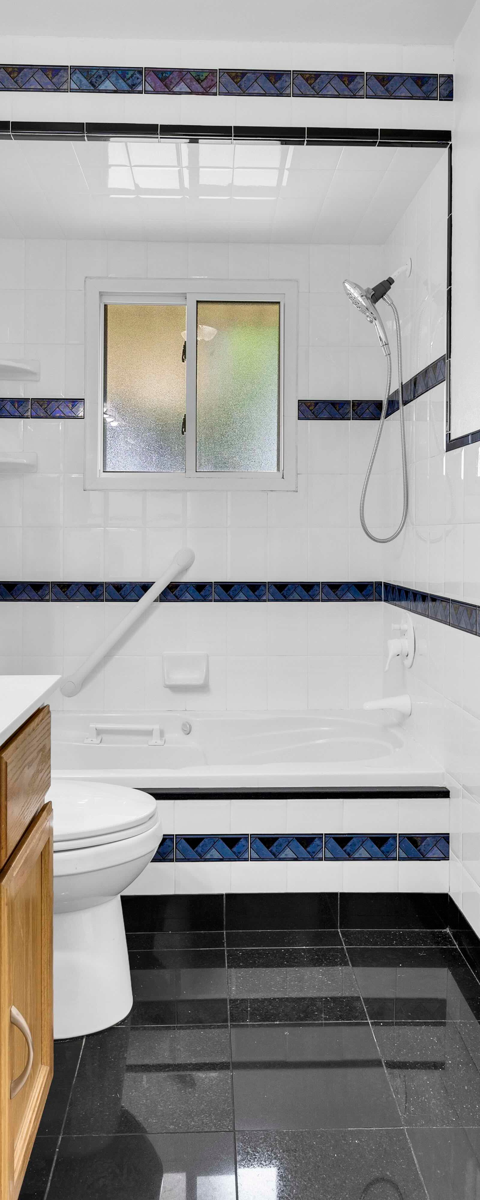 Bathroom with white tiles, blue trim, wood vanity, and a bathtub with double showerheads.