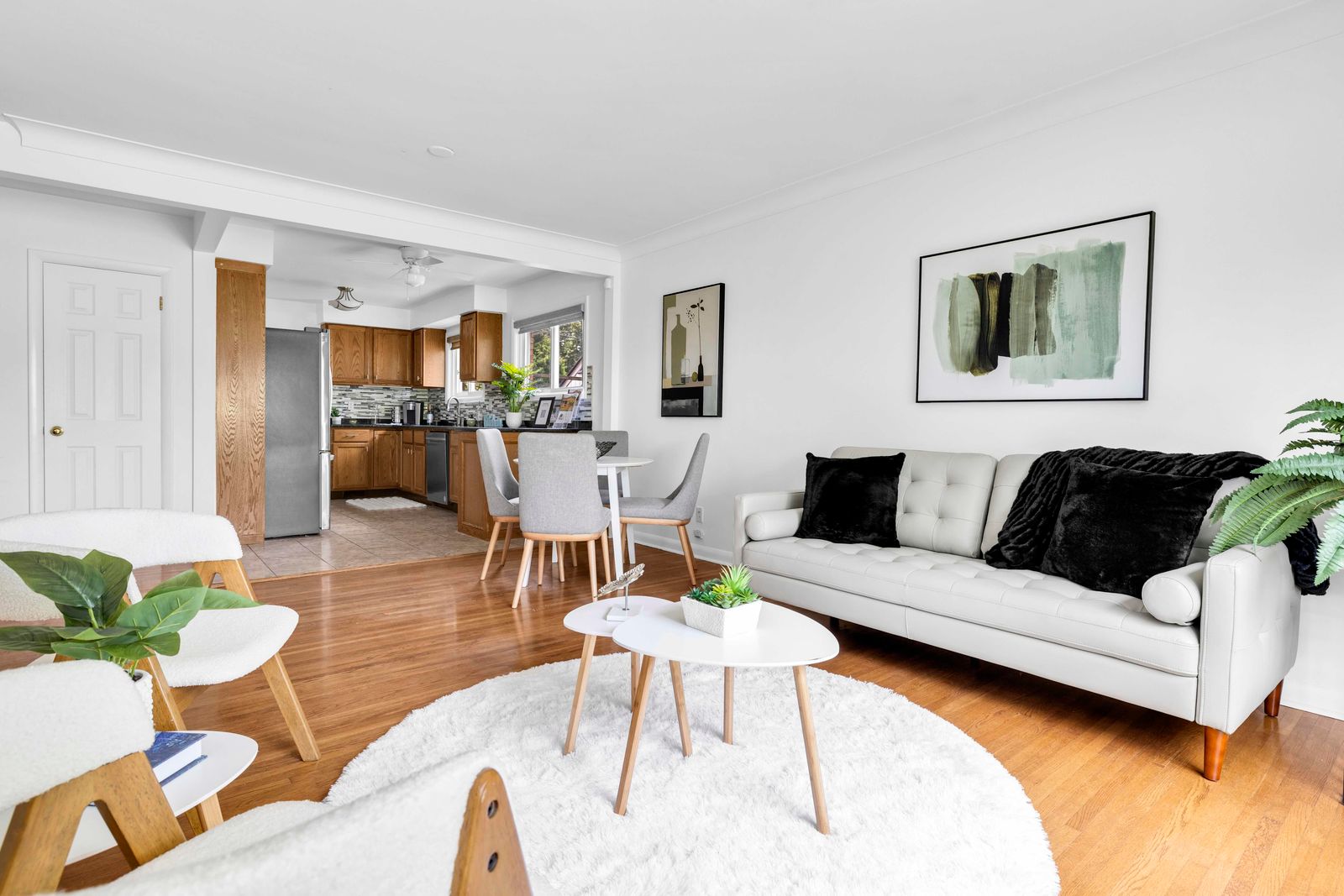 Bright living room with white and wooden furniture, dining area, and view of the kitchen.