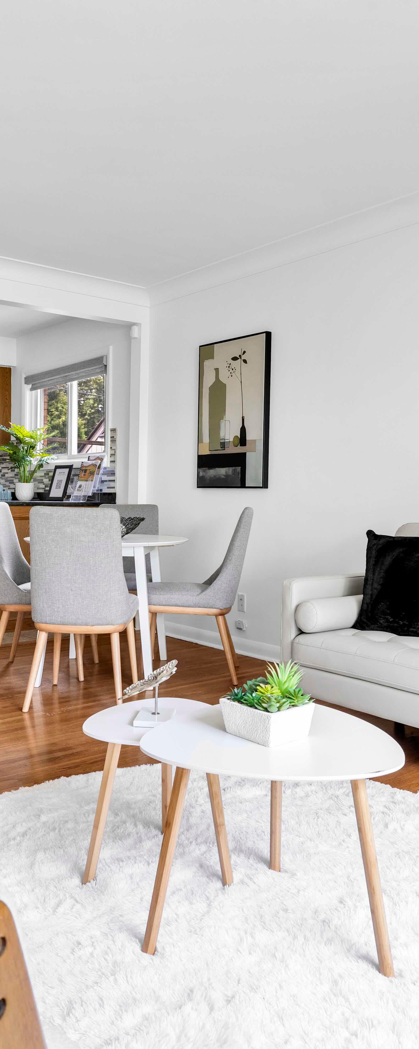 Bright living room with white and wooden furniture, dining area, and view of the kitchen.