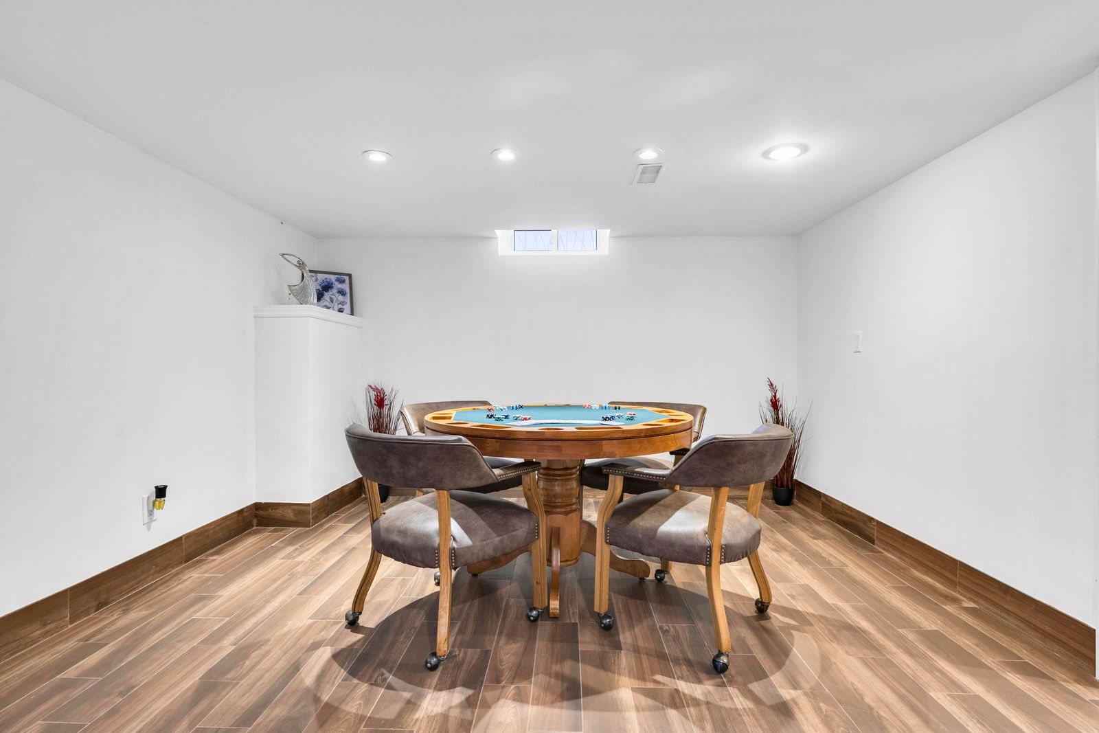Basement game area with poker table, rolling chairs, wood-look floor, and white walls.
