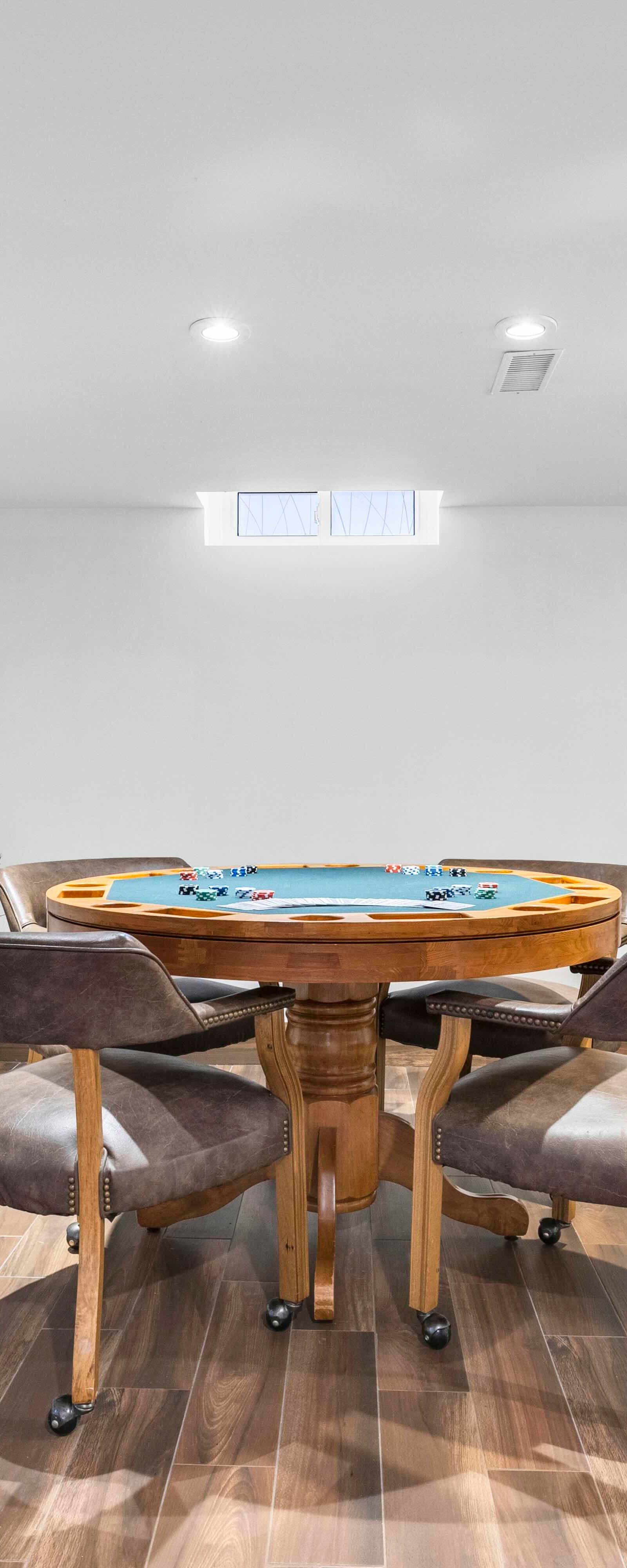 Basement game area with poker table, rolling chairs, wood-look floor, and white walls.