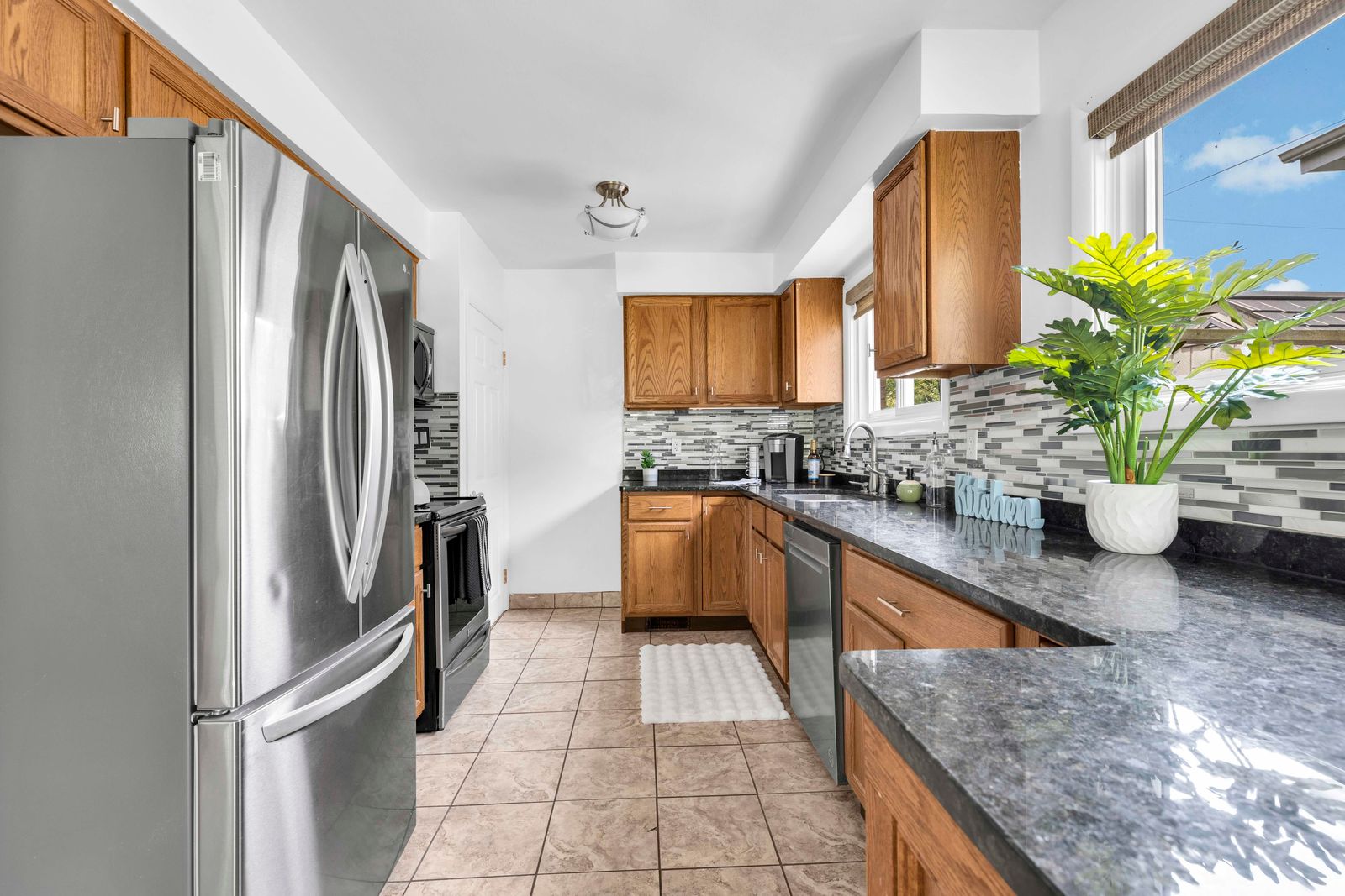 Kitchen view showing appliances, wooden cabinetry, tile floor, and window with outdoor view.