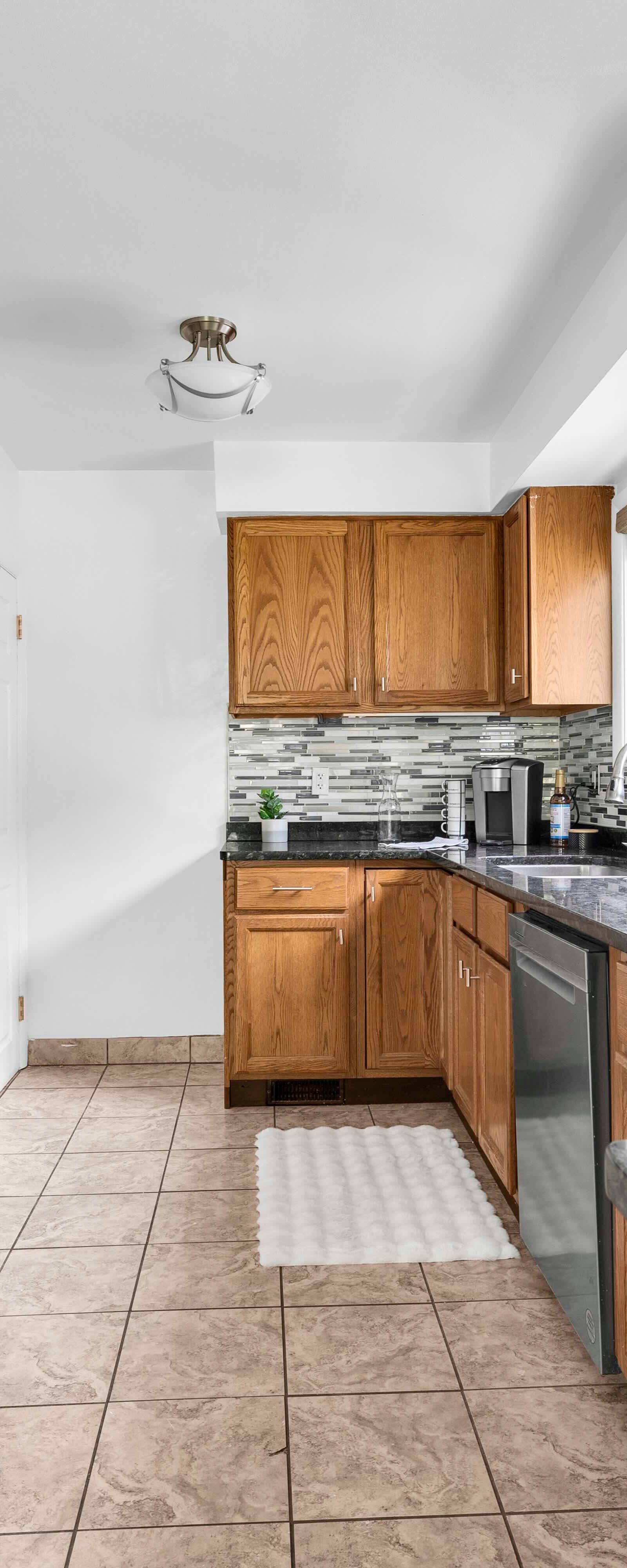 Kitchen view showing appliances, wooden cabinetry, tile floor, and window with outdoor view.