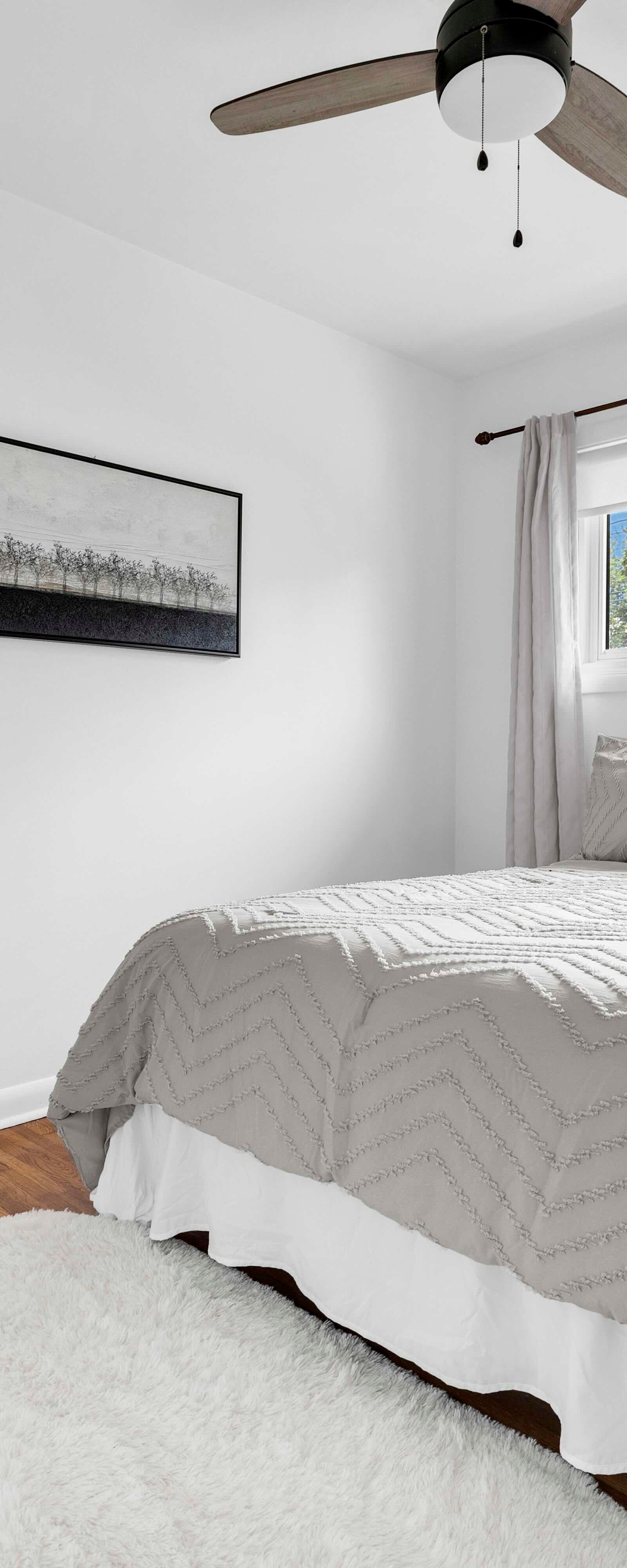 Bright bedroom with a bed, black tufted chair, white walls, and a ceiling fan.