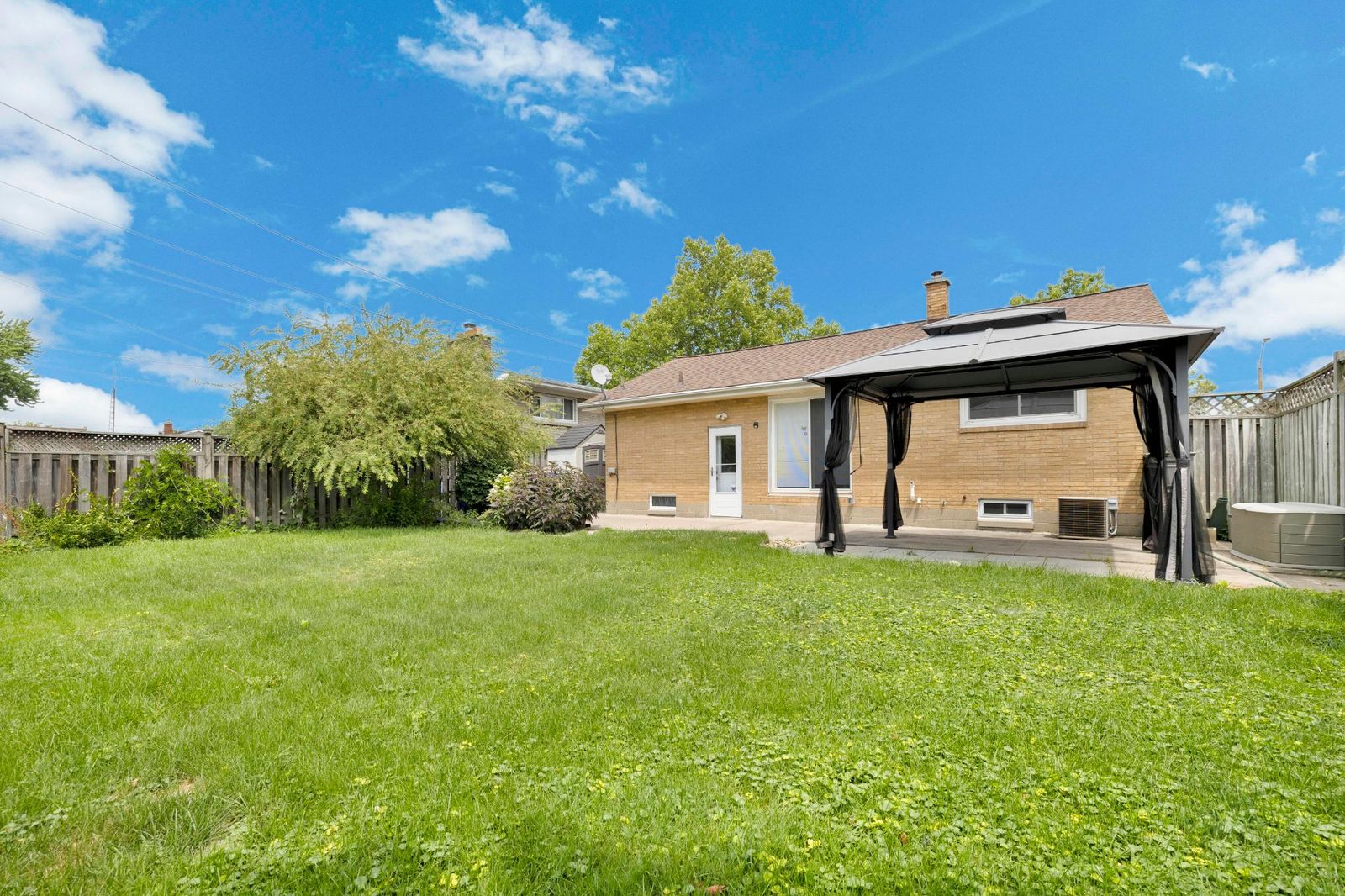 Backyard view showing brick rear exterior of the house, grassy lawn, and a gazebo on a paved patio.