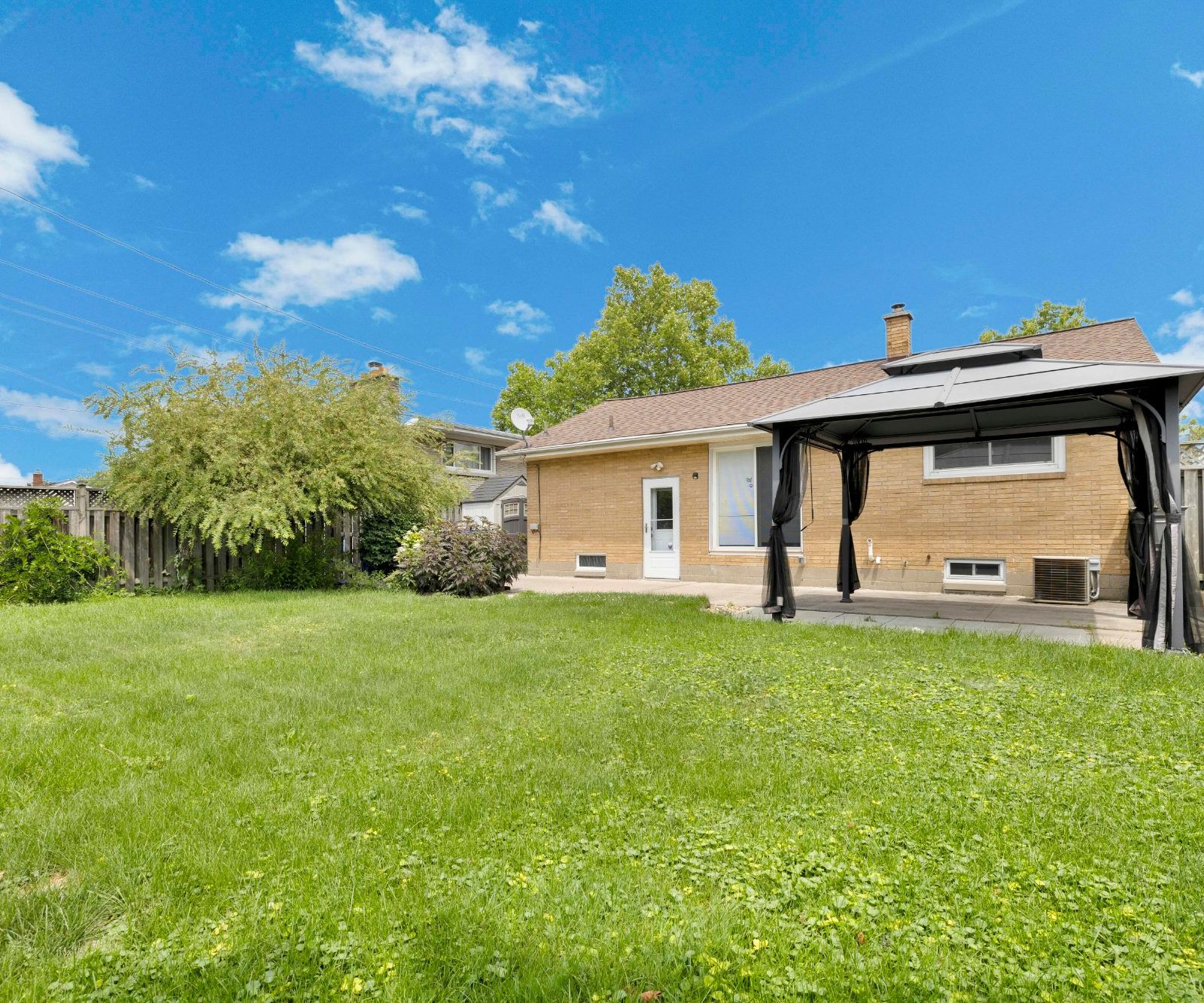 Backyard view showing brick rear exterior of the house, grassy lawn, and a gazebo on a paved patio.