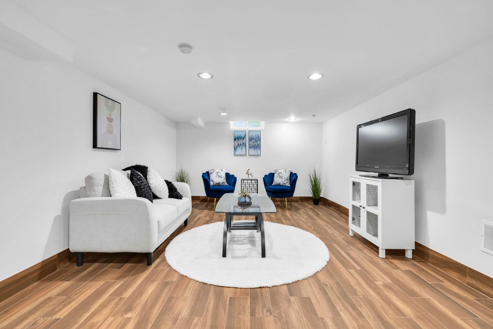 Basement living area featuring seating, a TV console, artwork, and wood-look flooring.
