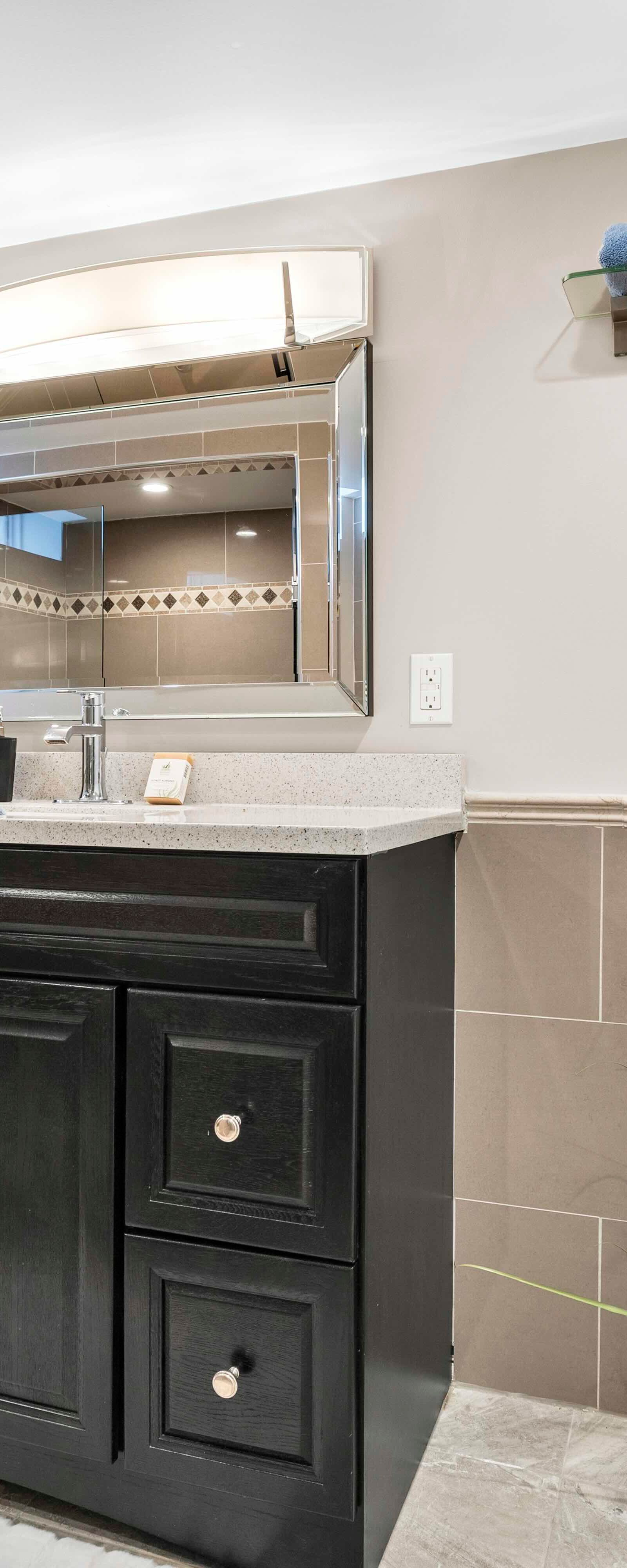 Bathroom vanity with framed mirror, toilet, and decorative plants with tiled walls and floor.