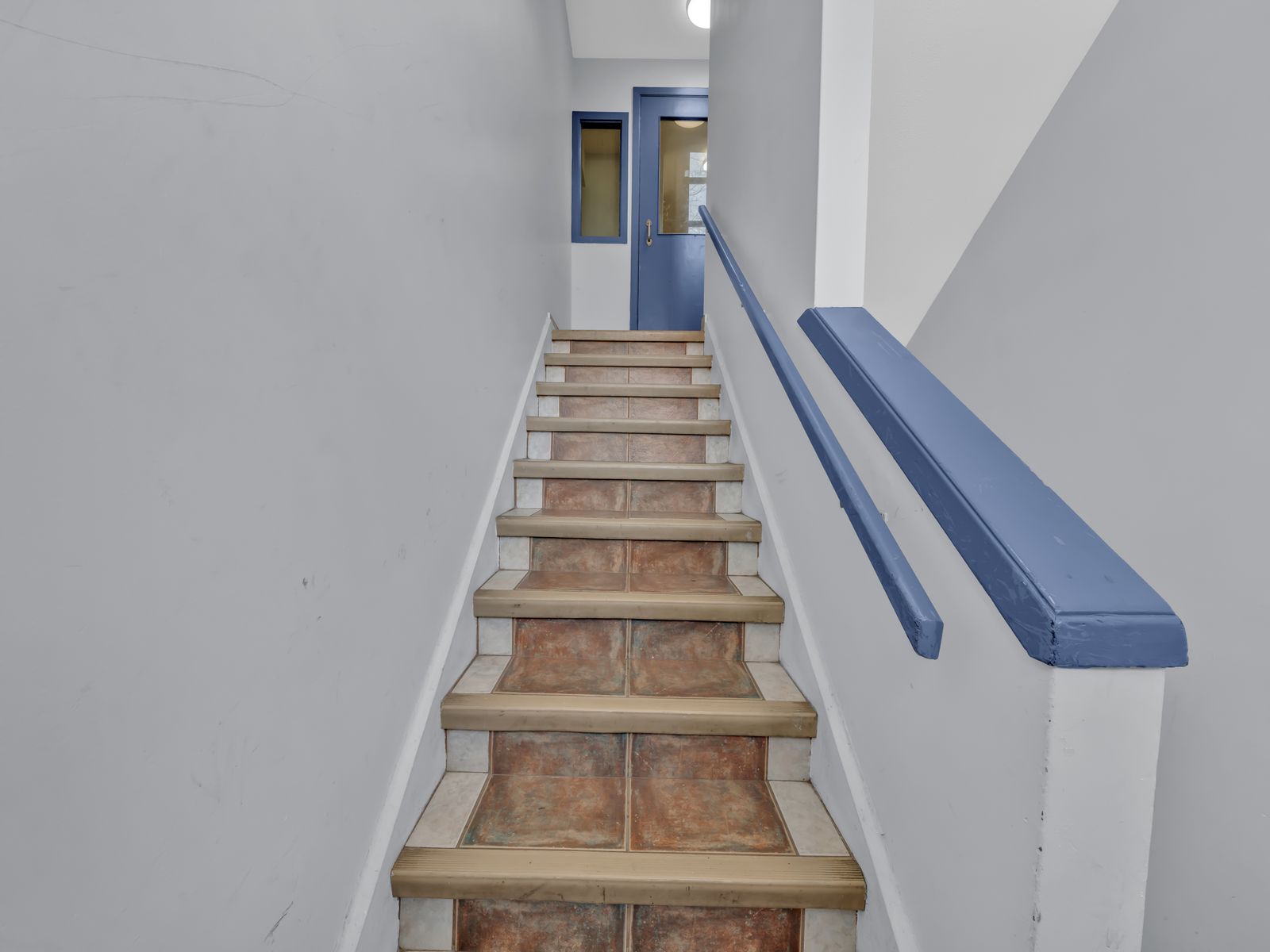 Tile staircase with blue handrail and blue door at top
