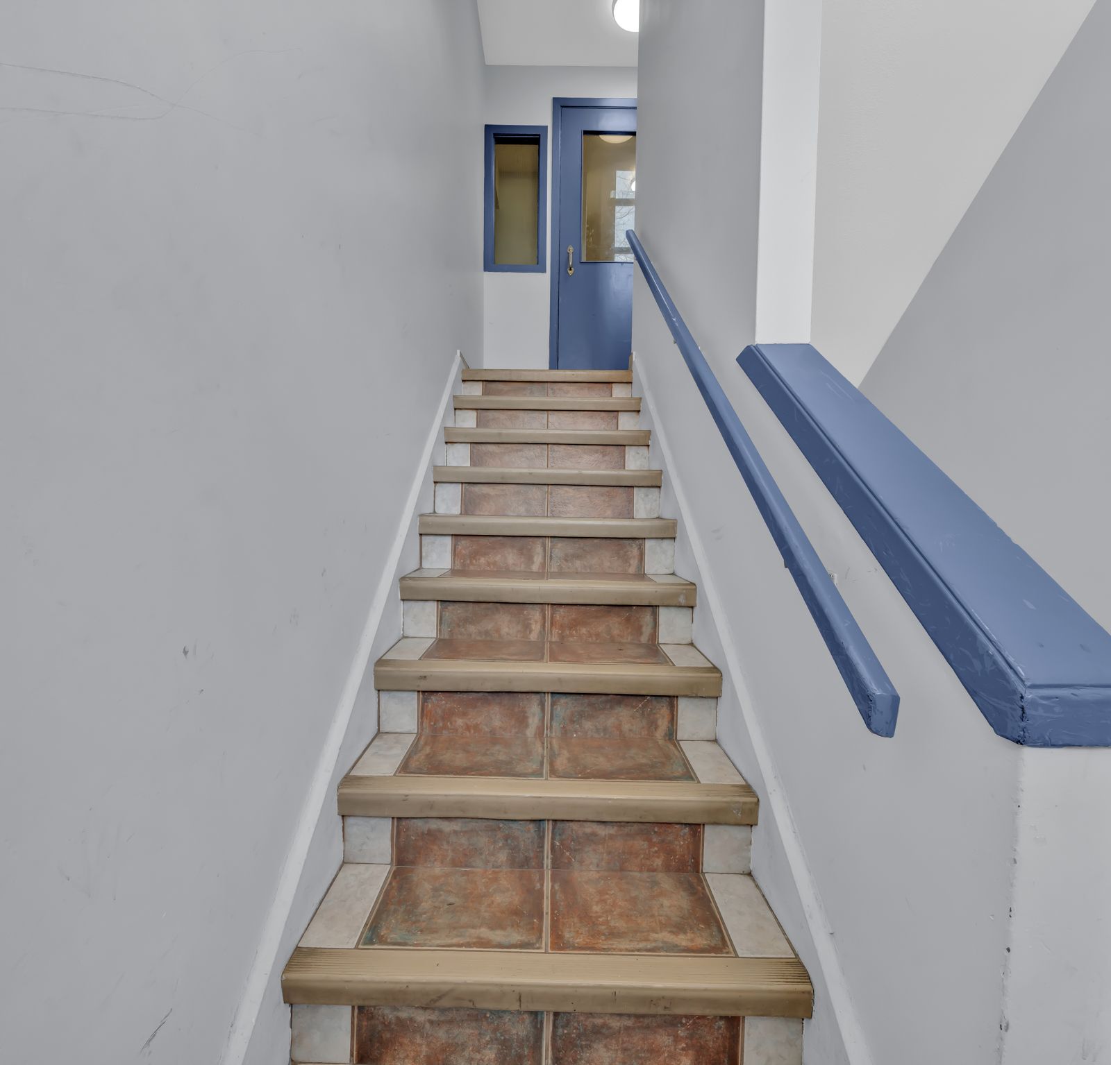 Tile staircase with blue handrail and blue door at top