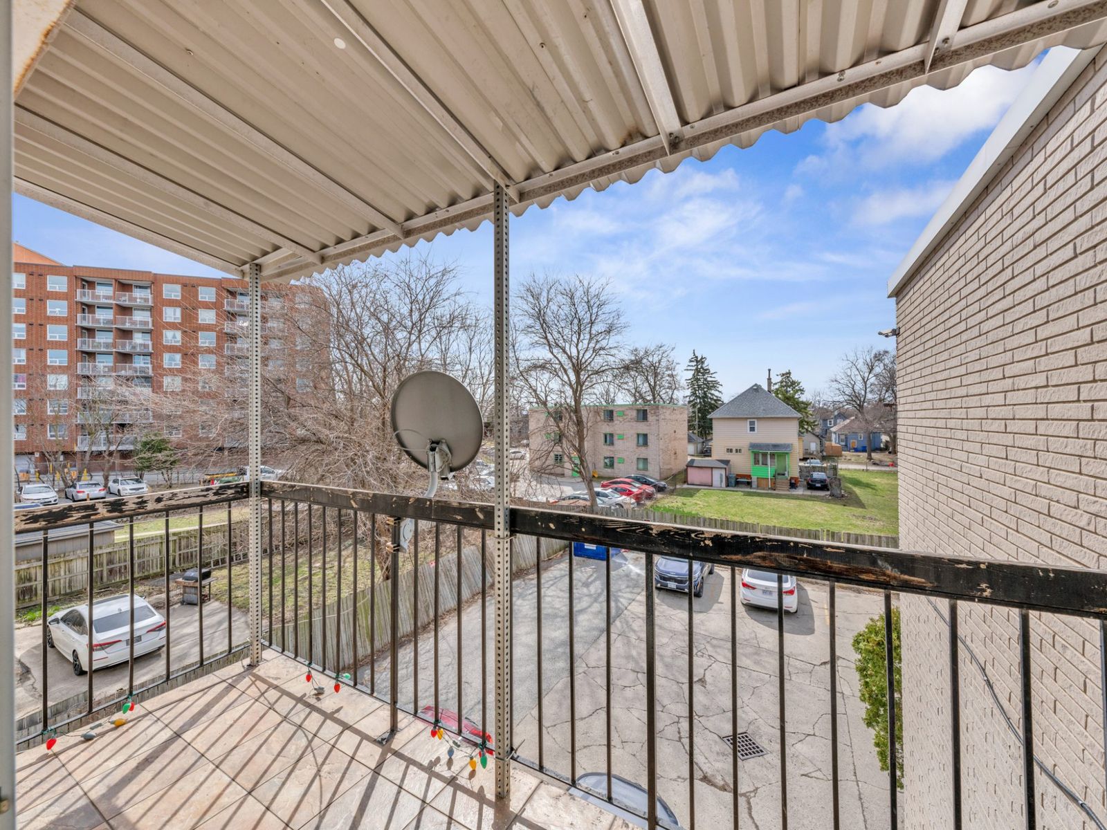 Balcony with metal railing overlooking parking area and surrounding buildings