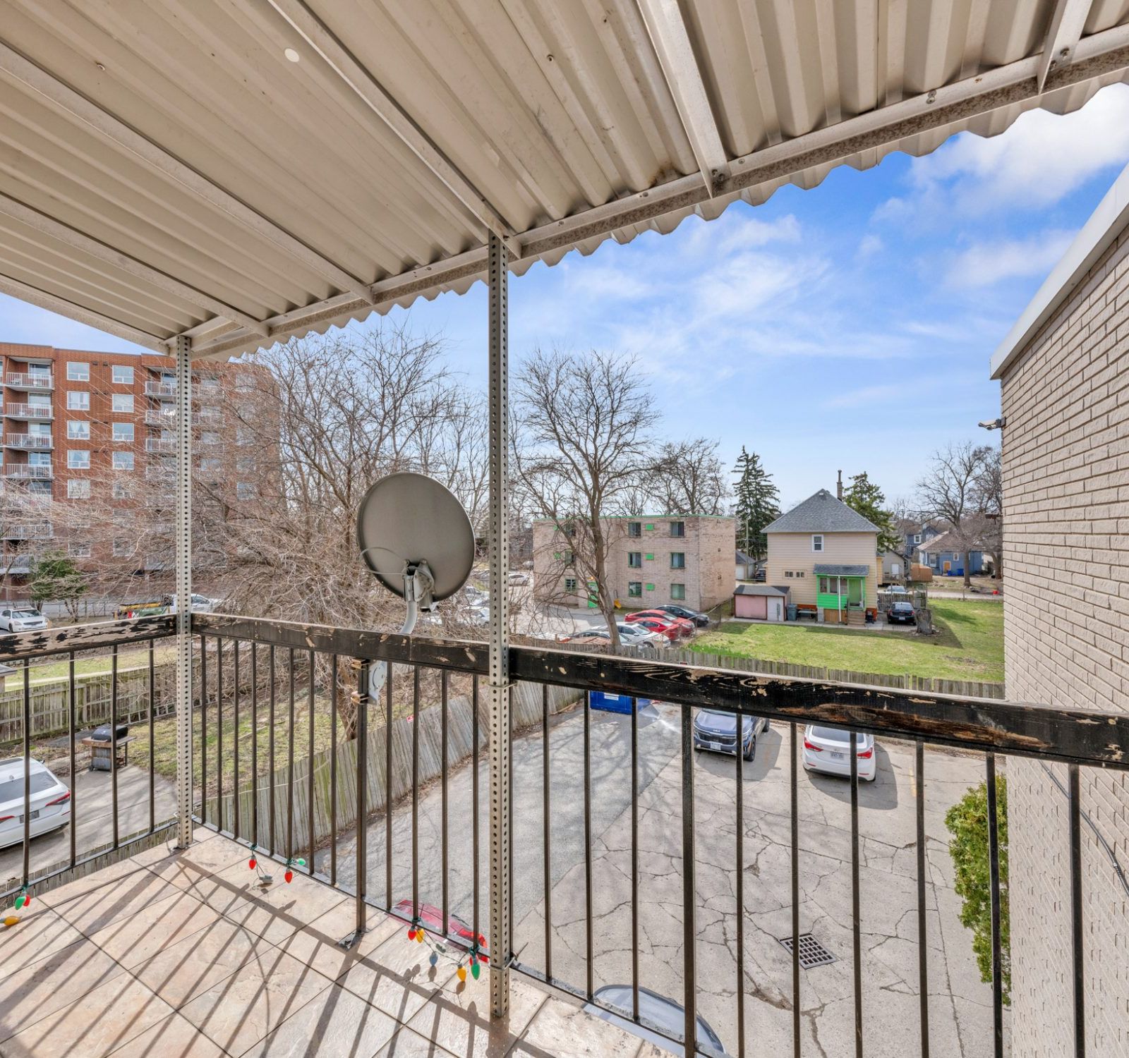 Balcony with metal railing overlooking parking area and surrounding buildings
