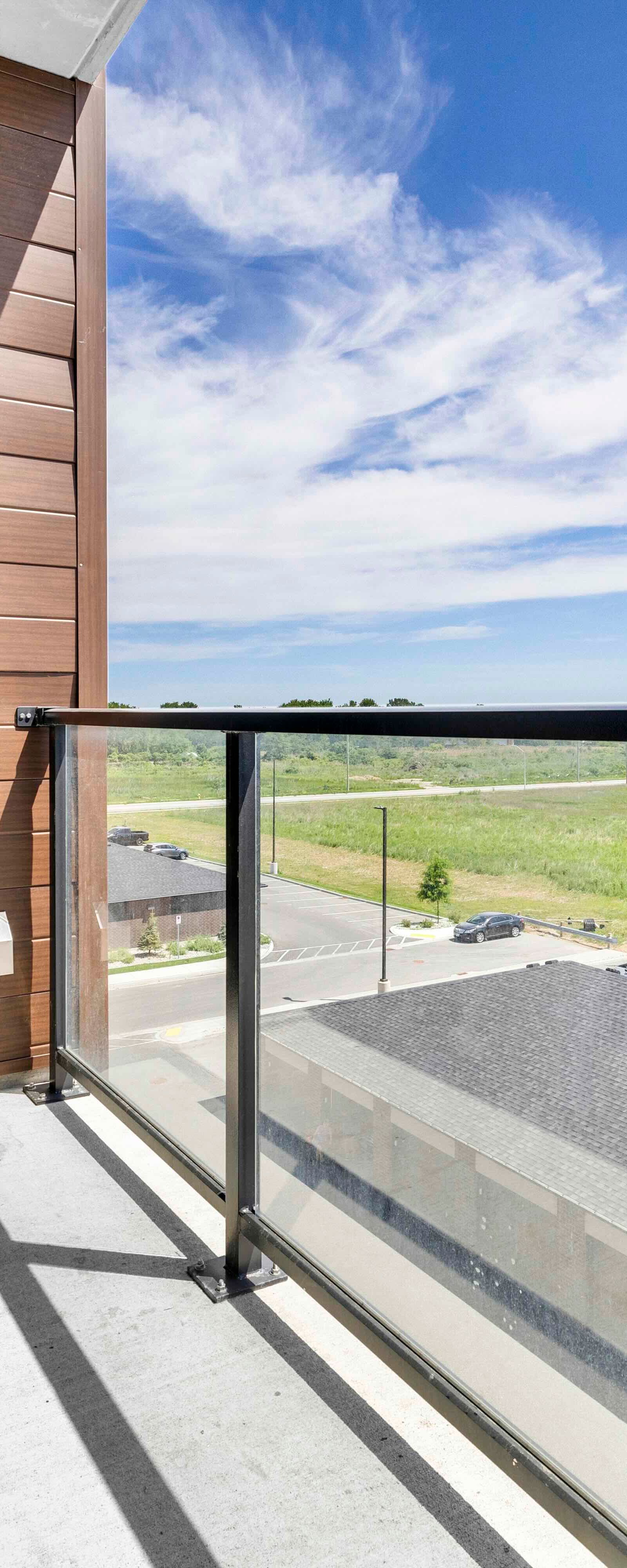 East-facing balcony with glass railing, black door, and wood-paneled wall under open sky