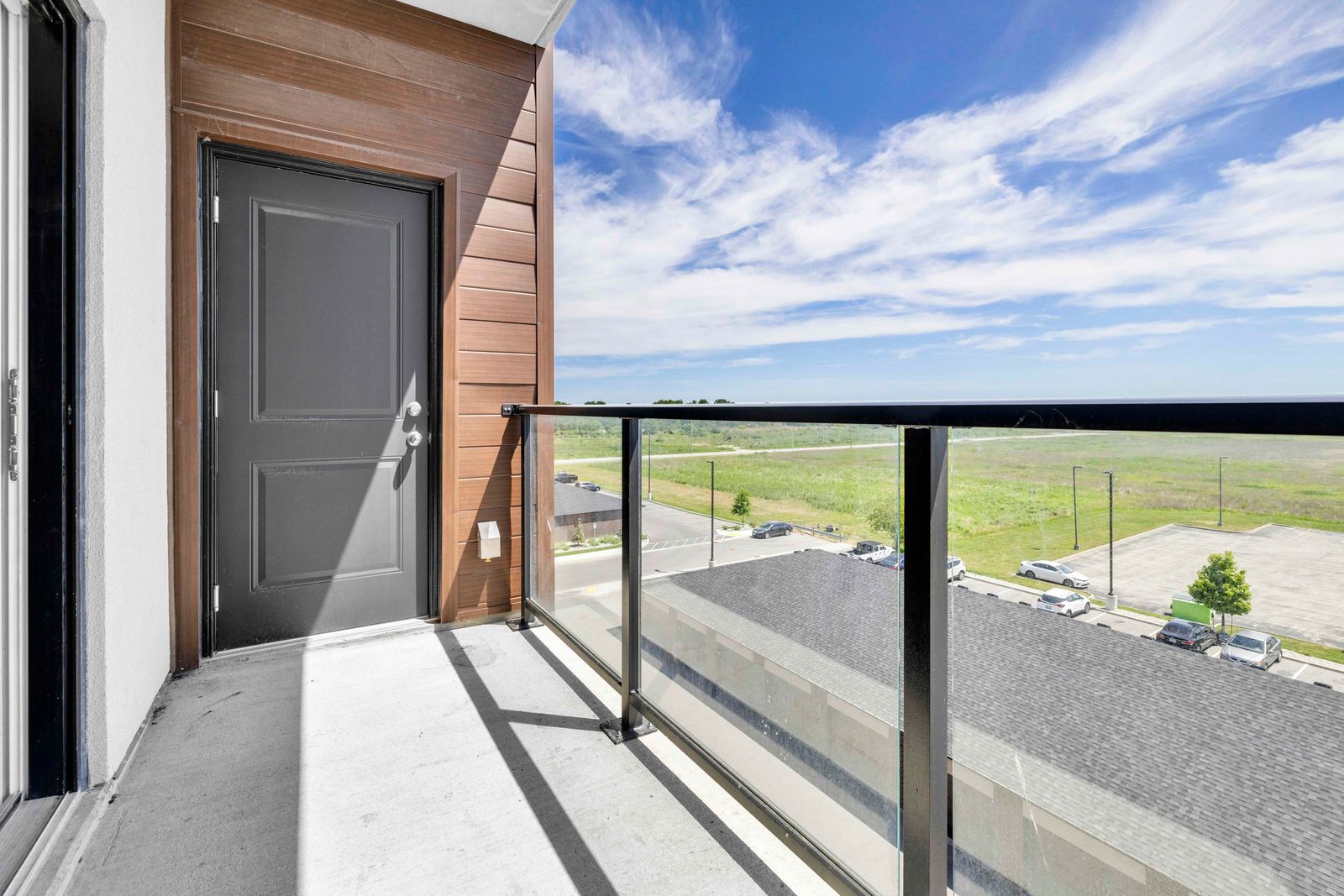 East-facing balcony with glass railing, black door, and wood-paneled wall under open sky