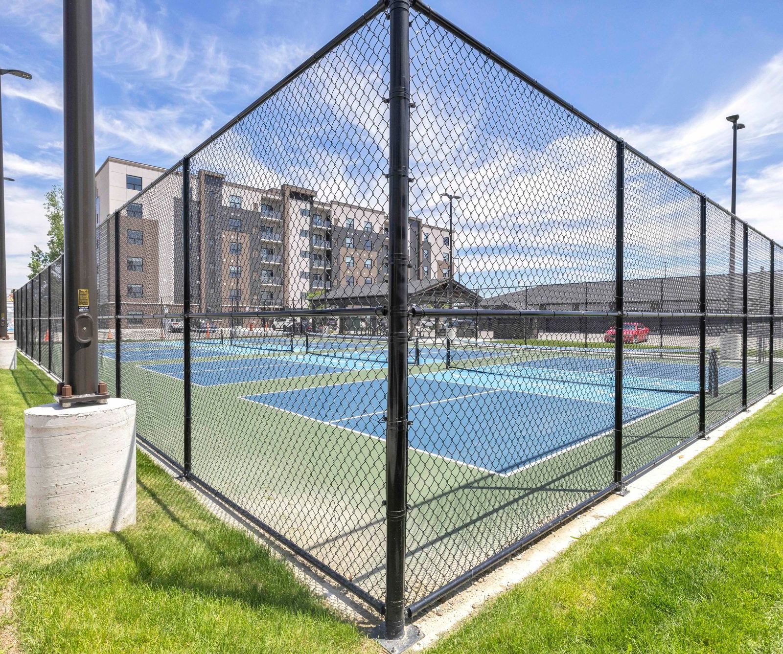 Fenced pickleball courts with grassy area and building in background