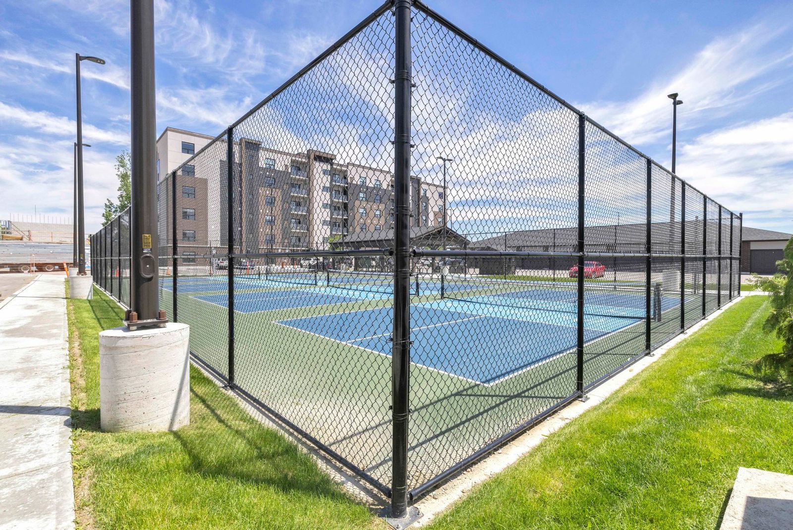 Fenced pickleball courts with grassy area and building in background