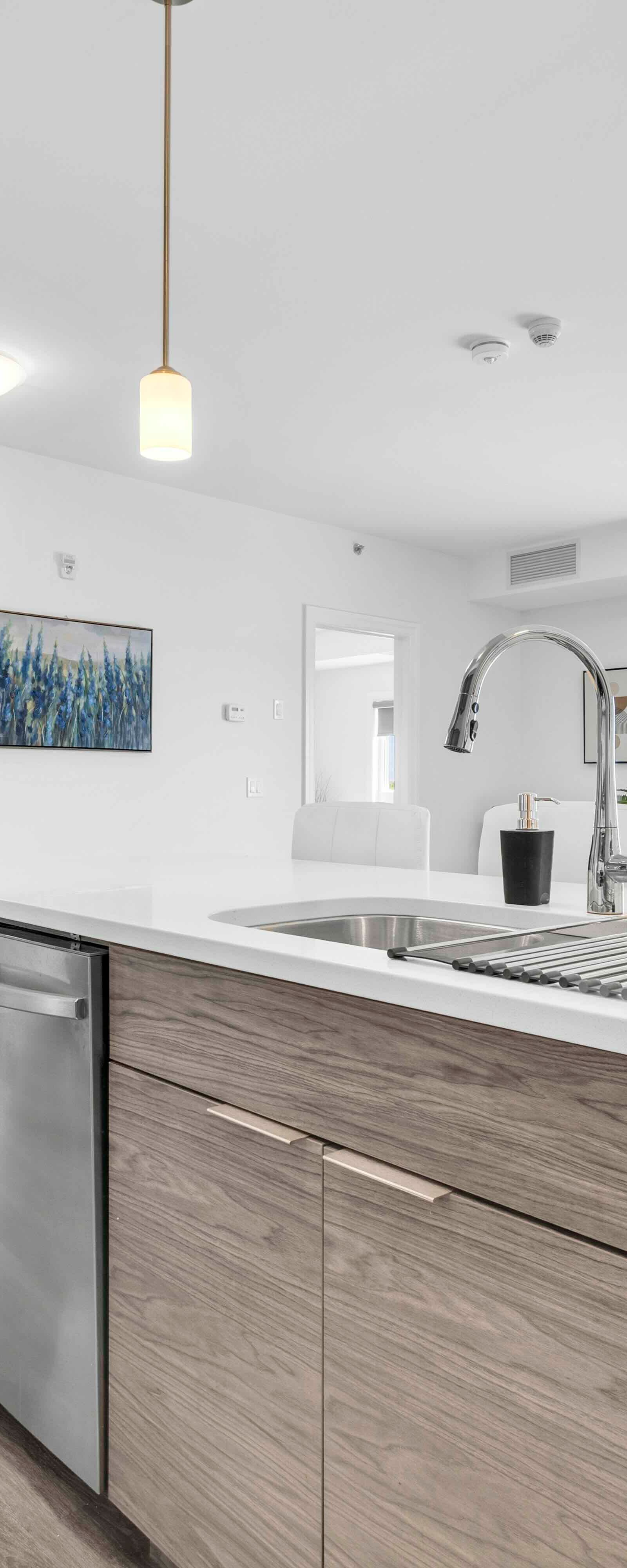 Kitchen island side angle with sink, dishwasher, and view to living area and balcony window