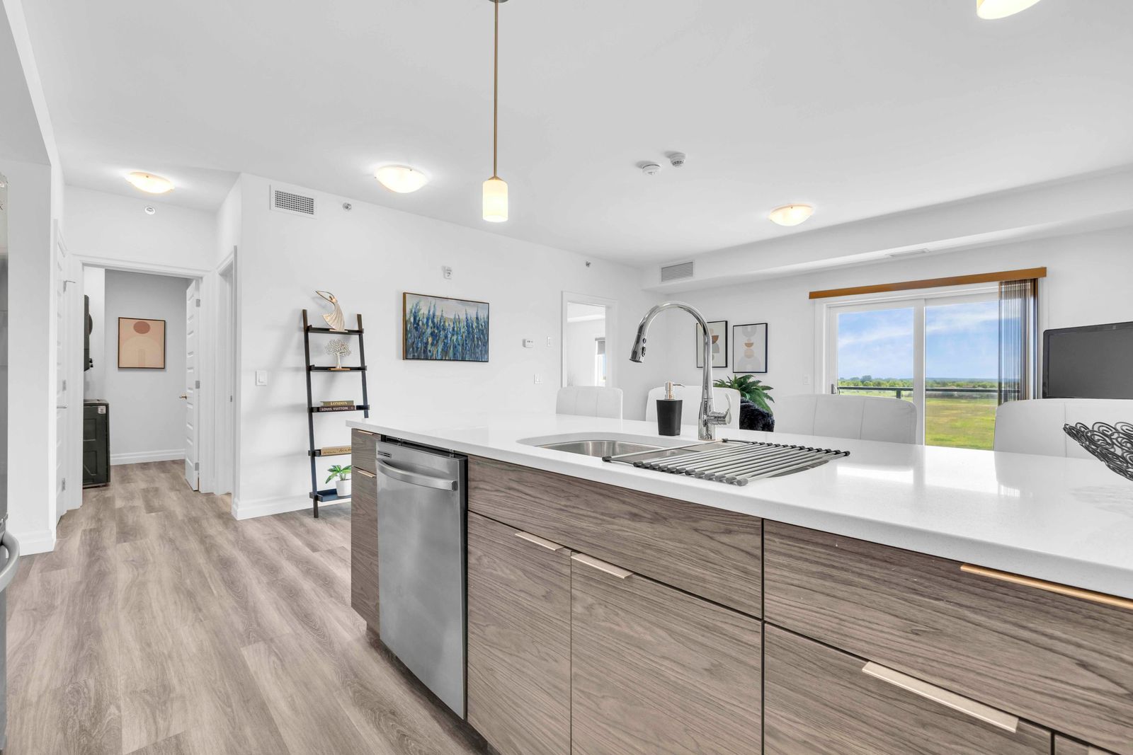 Kitchen island side angle with sink, dishwasher, and view to living area and balcony window
