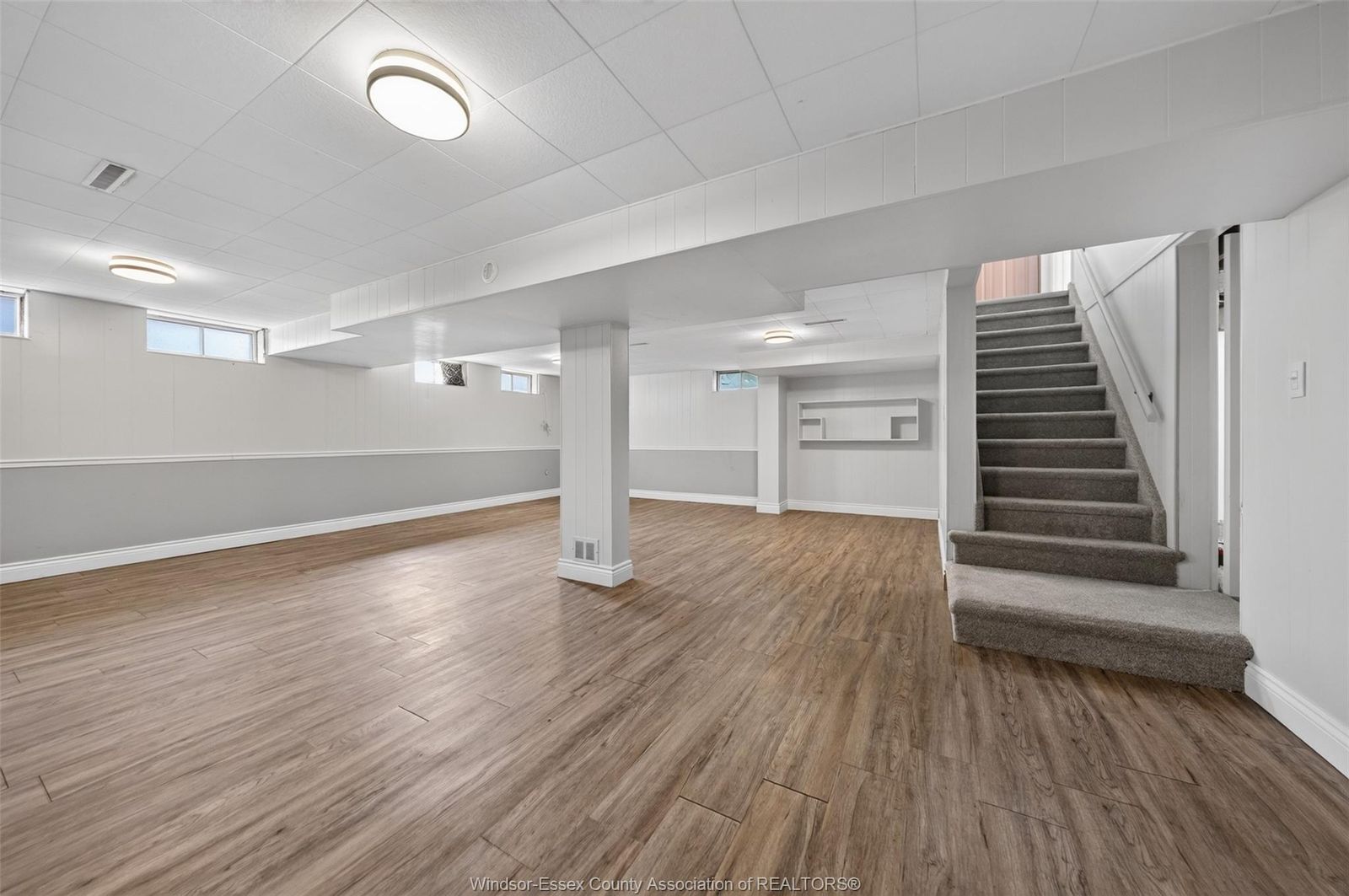 Bright finished basement with wood-look flooring, small windows and carpeted stairs