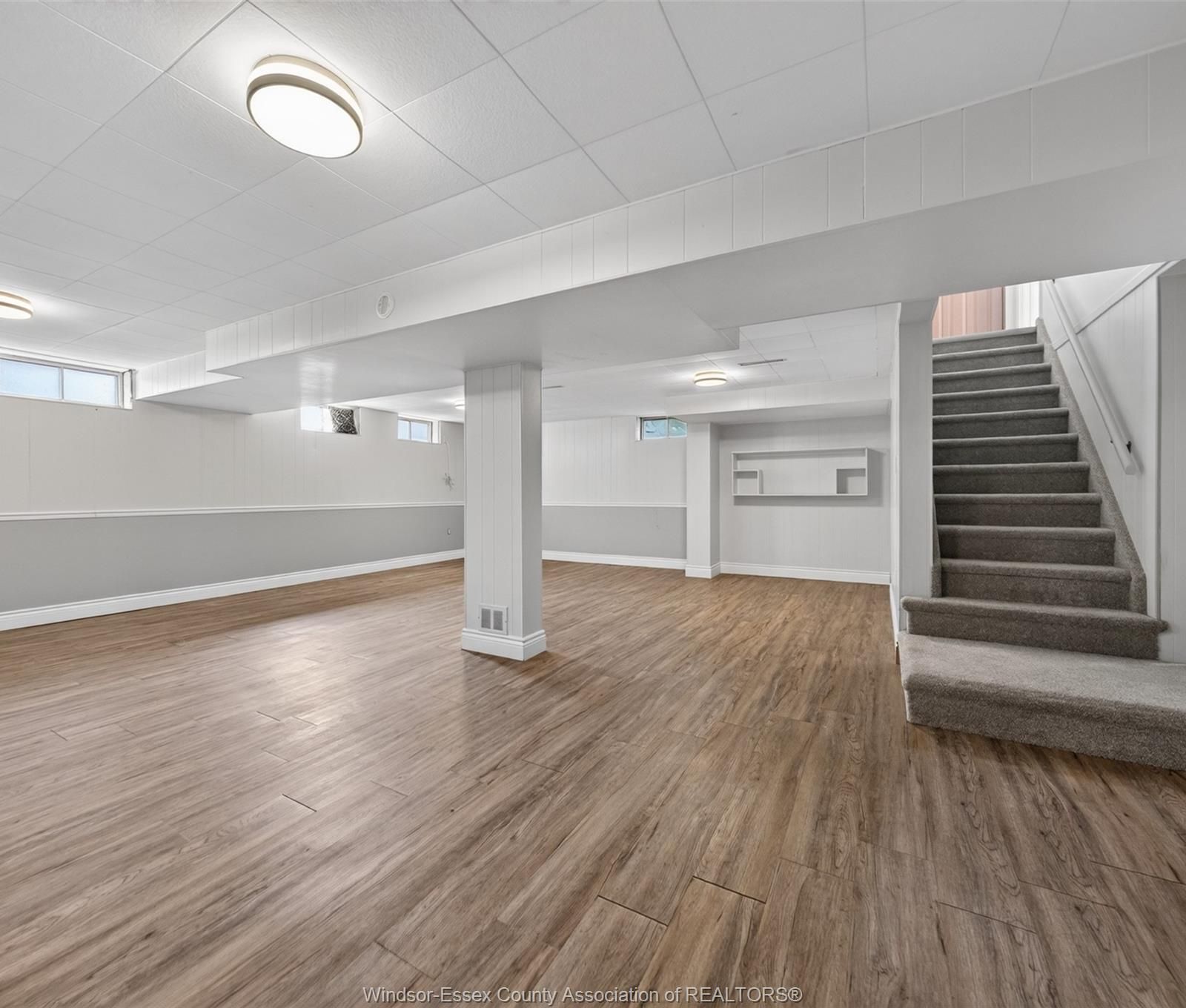 Bright finished basement with wood-look flooring, small windows and carpeted stairs
