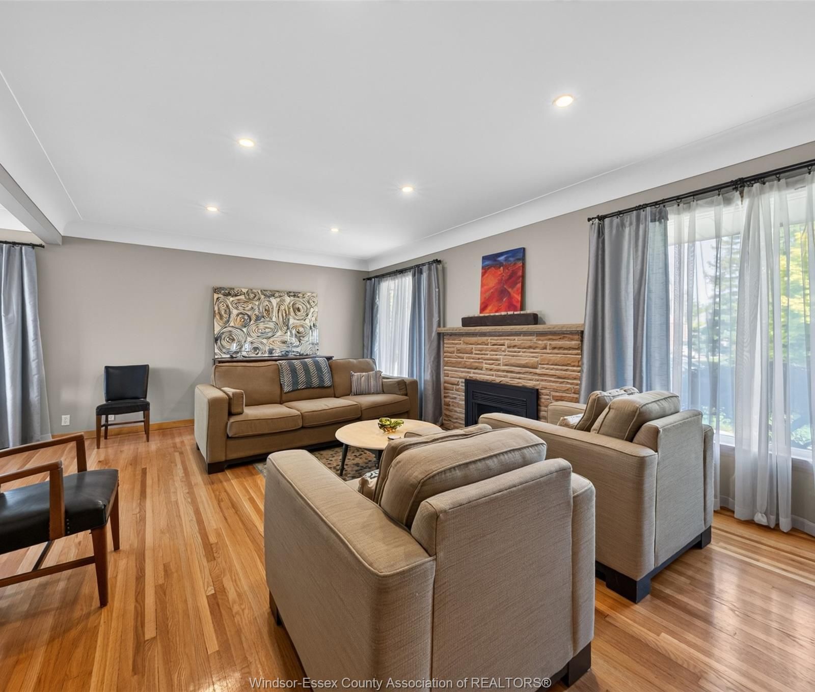 Living room seating grouped near the stone fireplace with large curtained windows