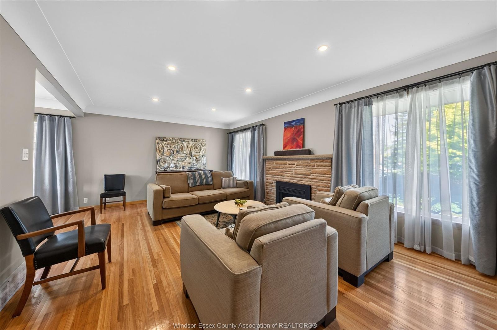 Living room seating grouped near the stone fireplace with large curtained windows